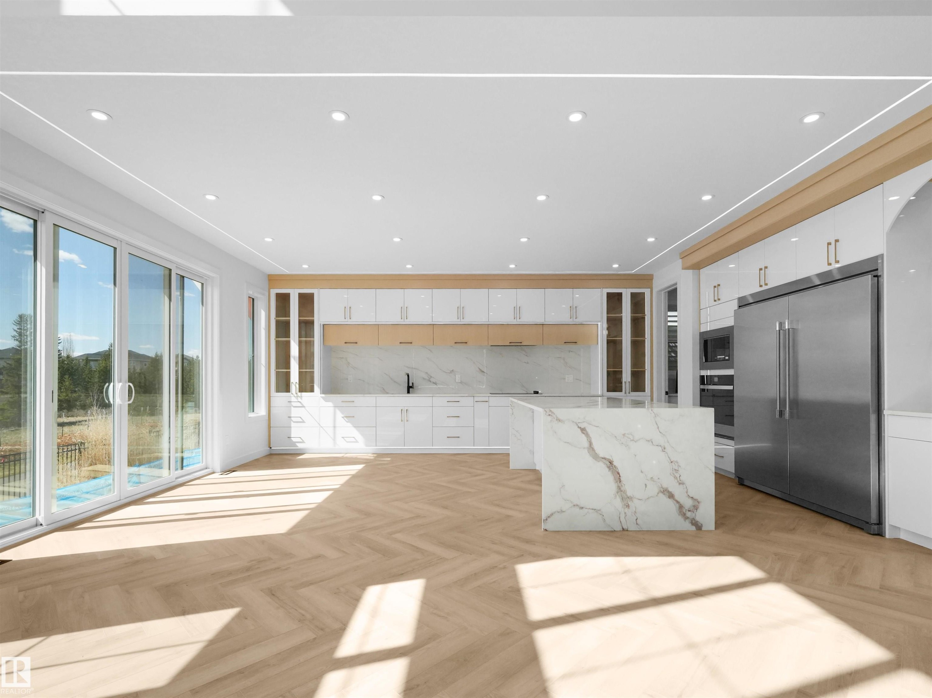Contemporary kitchen featuring herringbone wood-finish flooring, white cabinetry with gold-tone hardware, a large waterfall island with veined stone, stainless steel appliances, and integrated recessed lighting - 2070 Collip Crescent Sw, Edmonton, AB - Indoor