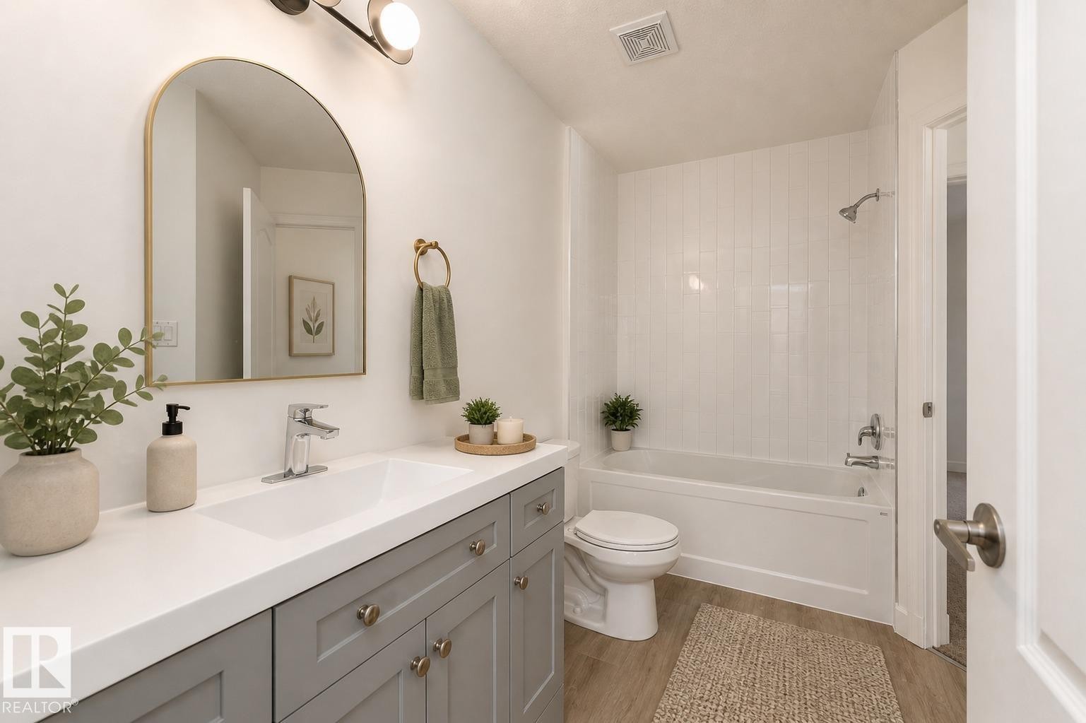Bathroom with wood-finish flooring, a white vanity countertop, gray cabinetry, and an arched wall mirror - #63 1033 Youville Dr W Nw, Edmonton, AB - Indoor Photo Showing Bathroom