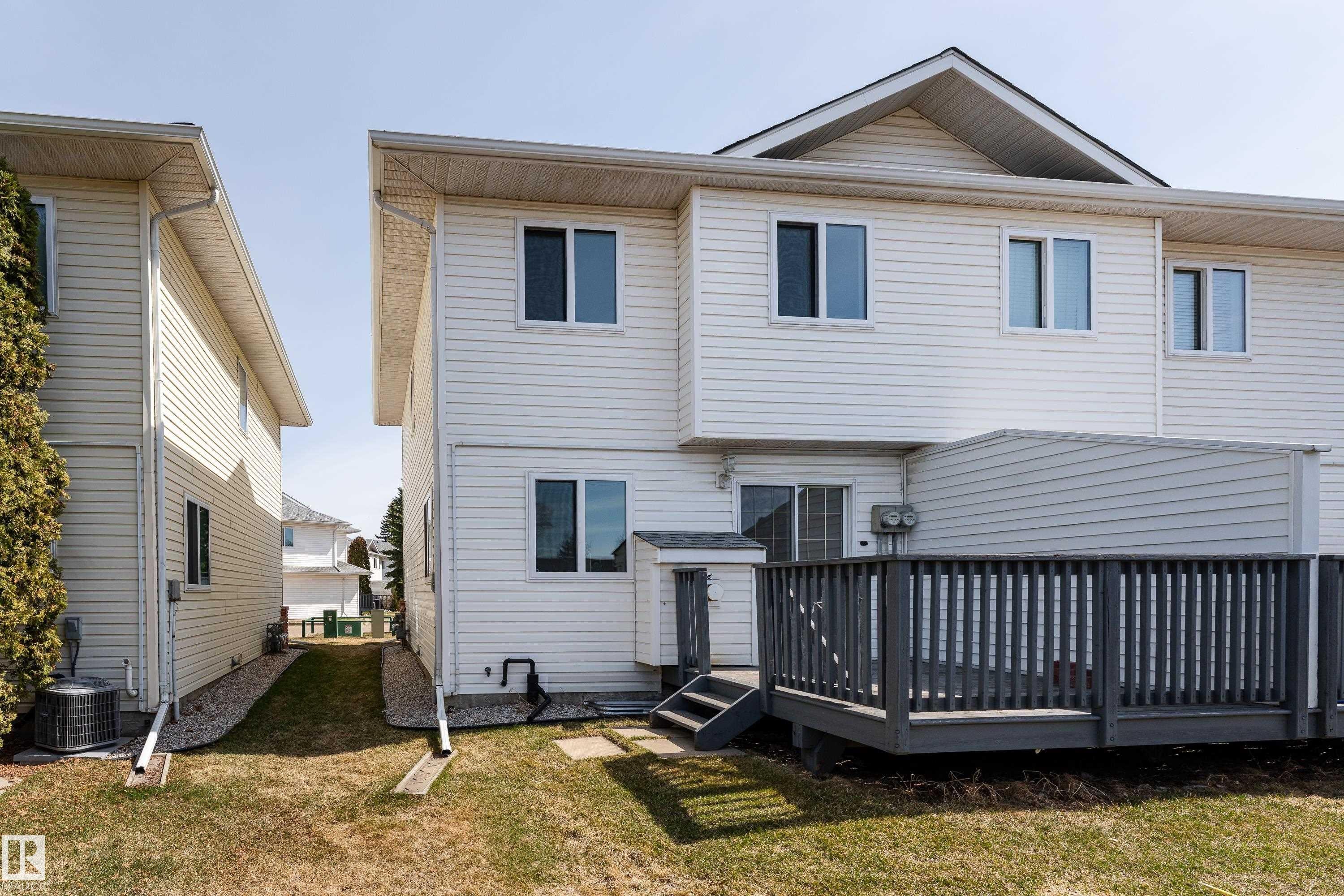 Rear exterior featuring a spacious wooden deck with railings, white vinyl siding, multiple windows, and a sliding glass door - #63 1033 Youville Dr W Nw, Edmonton, AB - Outdoor With Exterior
