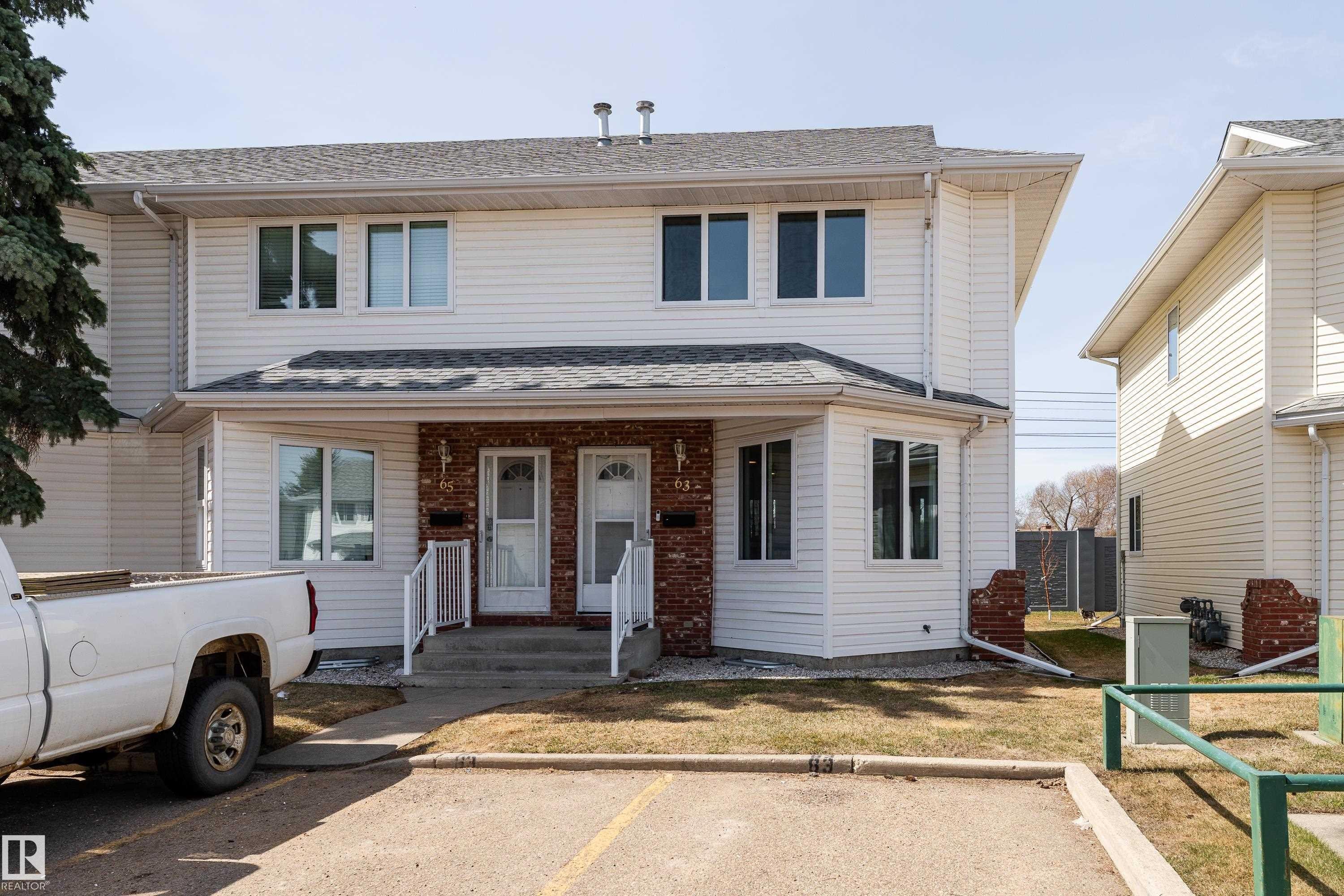 Duplex exterior featuring white siding and brick accents - #63 1033 Youville Dr W Nw, Edmonton, AB - Outdoor