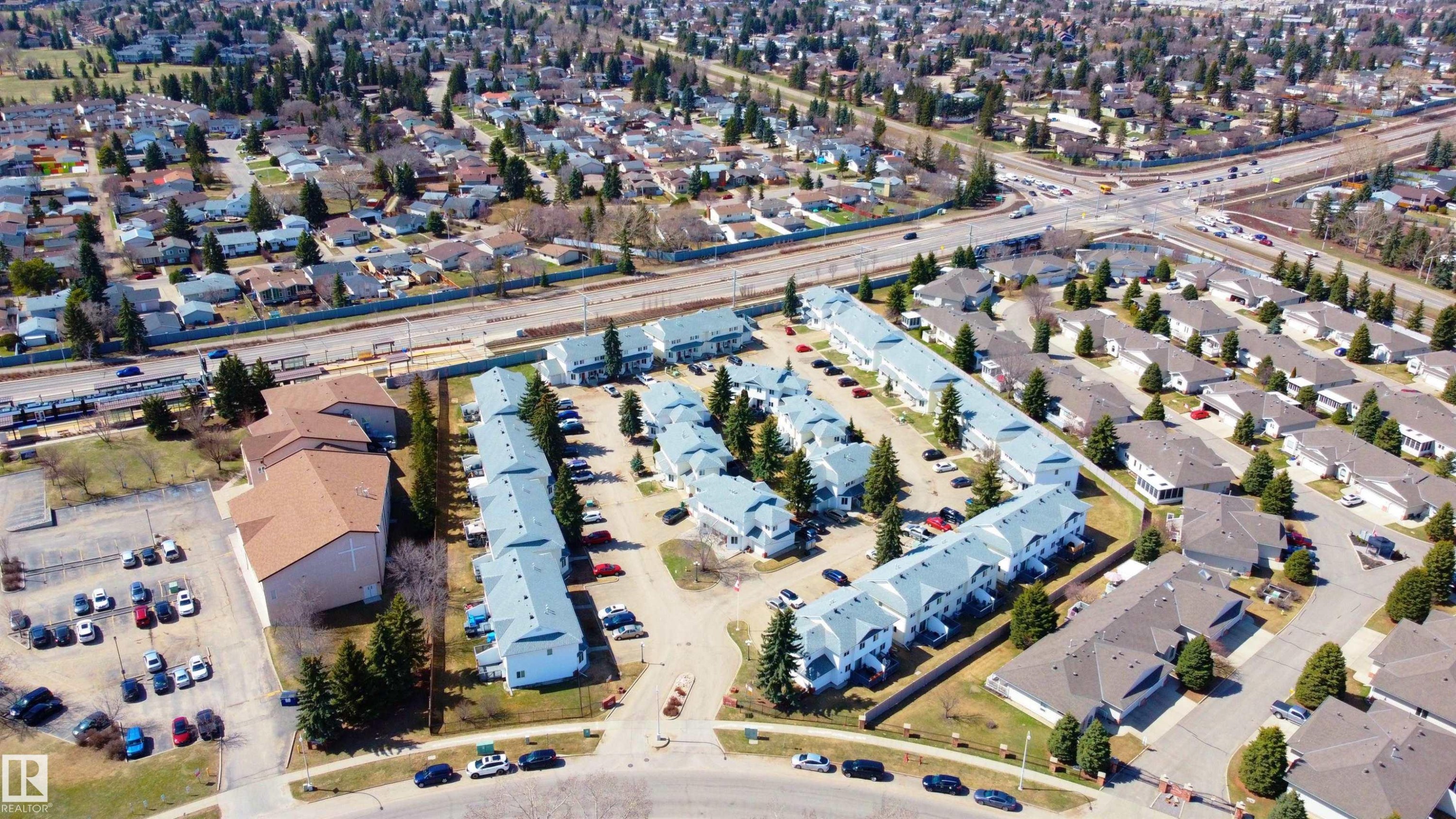 Residential development featuring multiple townhouse-style buildings with light-colored siding and grey roofing - #63 1033 Youville Dr W Nw, Edmonton, AB - Outdoor With View