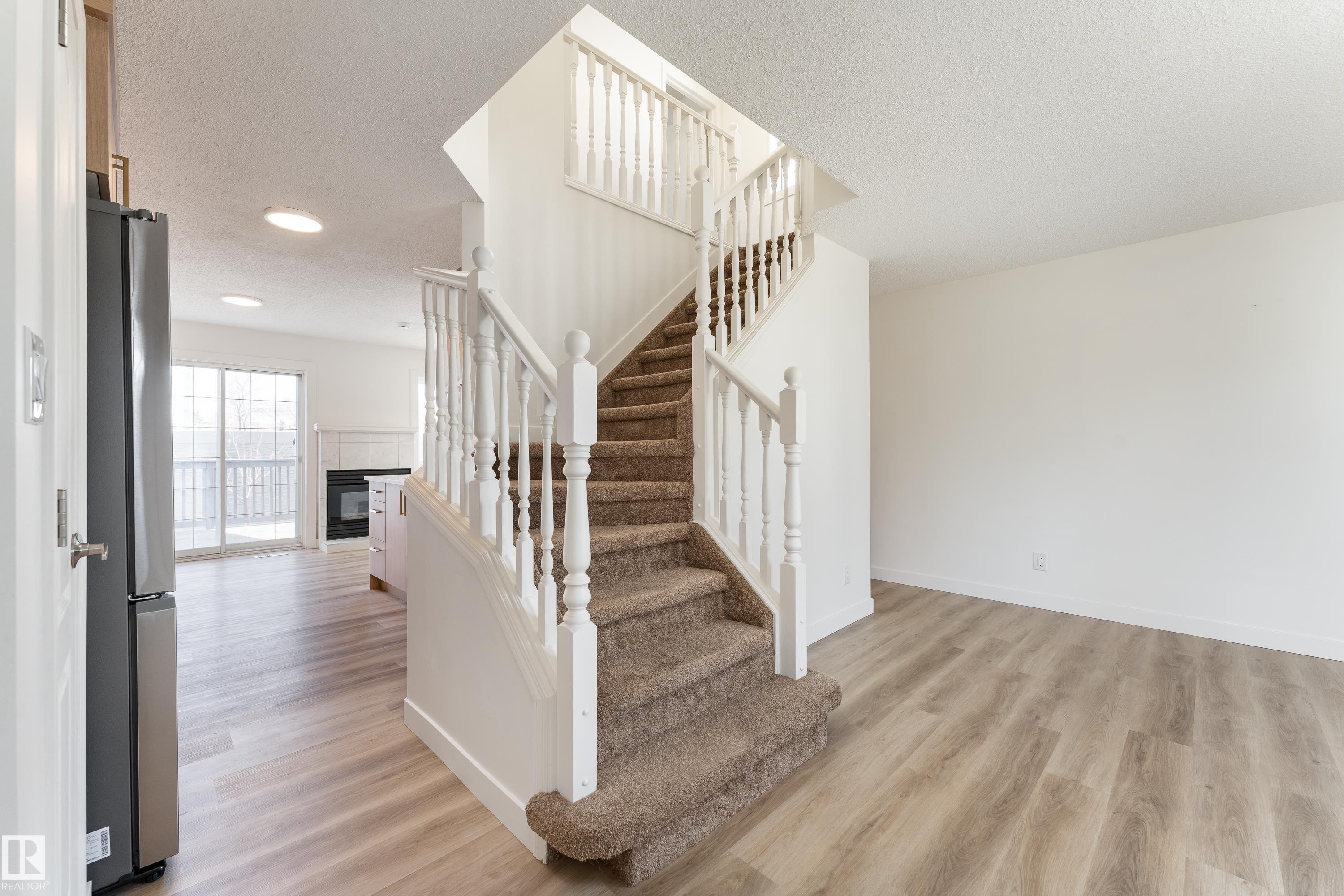 Staircase with carpeted treads and white wood balusters, complemented by light wood-finish flooring - #63 1033 Youville Dr W Nw, Edmonton, AB - Indoor Photo Showing Other Room