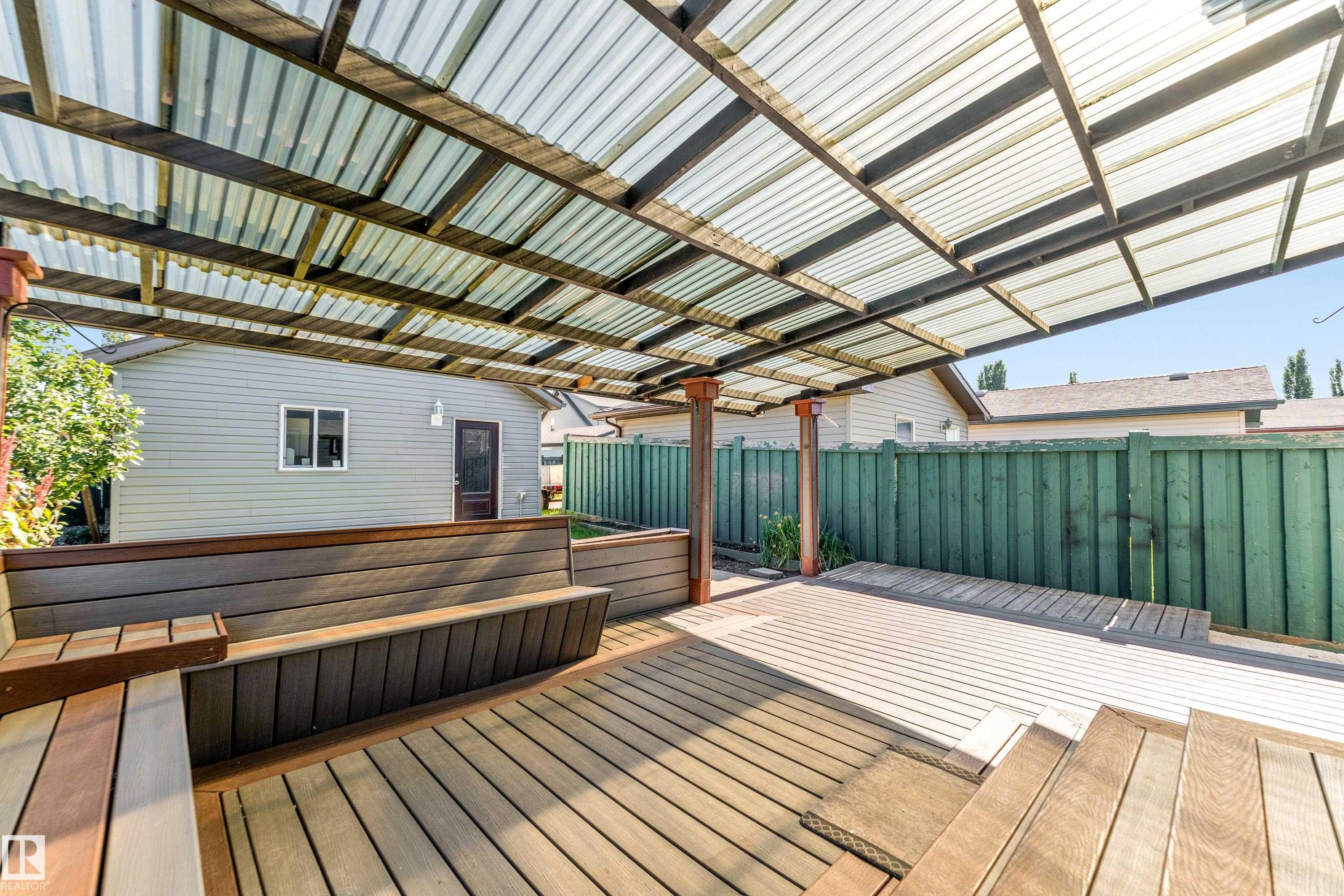 Outdoor covered deck featuring wood-finish decking, built-in benches, and a translucent corrugated roof - 1921 119A Street, Edmonton, AB