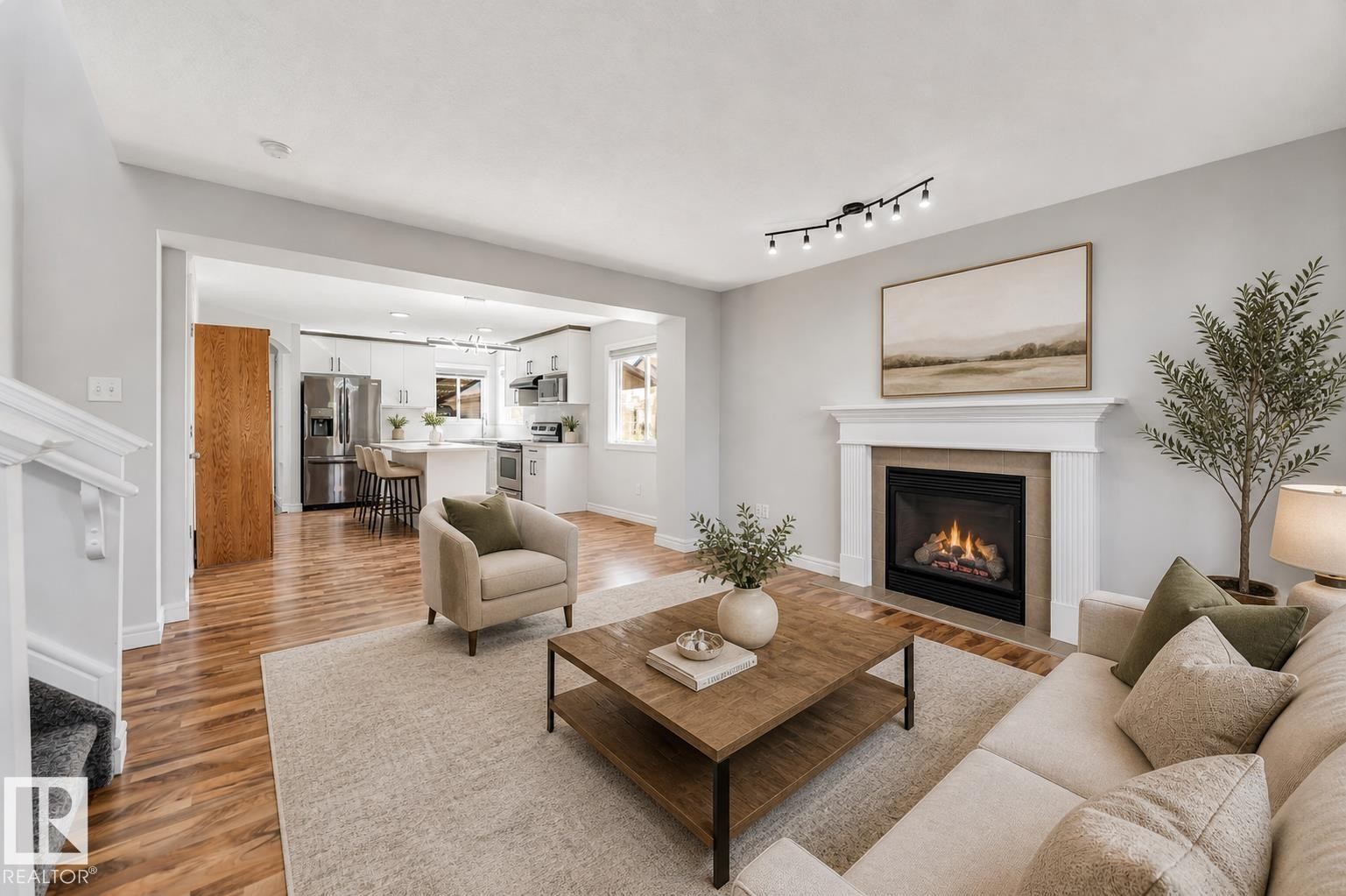 Open-concept living space featuring wood-finish flooring, a contemporary fireplace with a white mantel, and track lighting - 1921 119A Street, Edmonton, AB