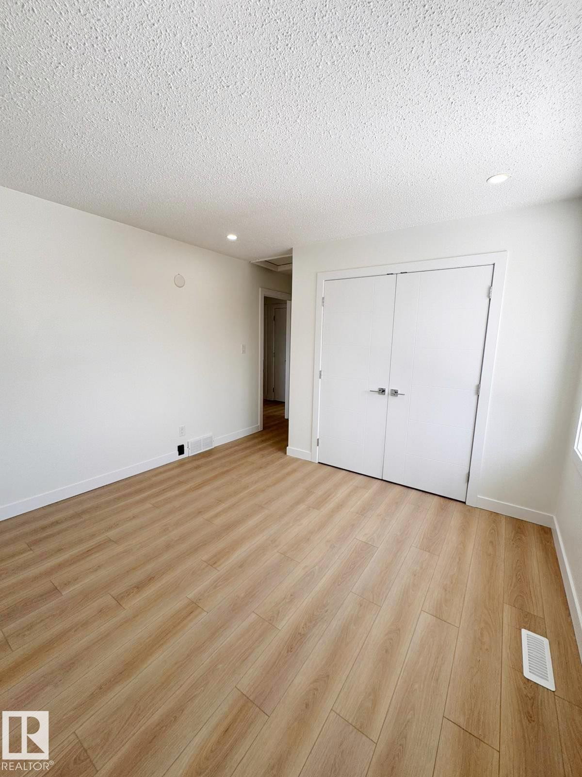 Bright interior room with wood-finish flooring, recessed lighting, white walls, and built-in double closet doors - 20 Hunt Road, Edmonton, AB - Indoor Photo Showing Other Room