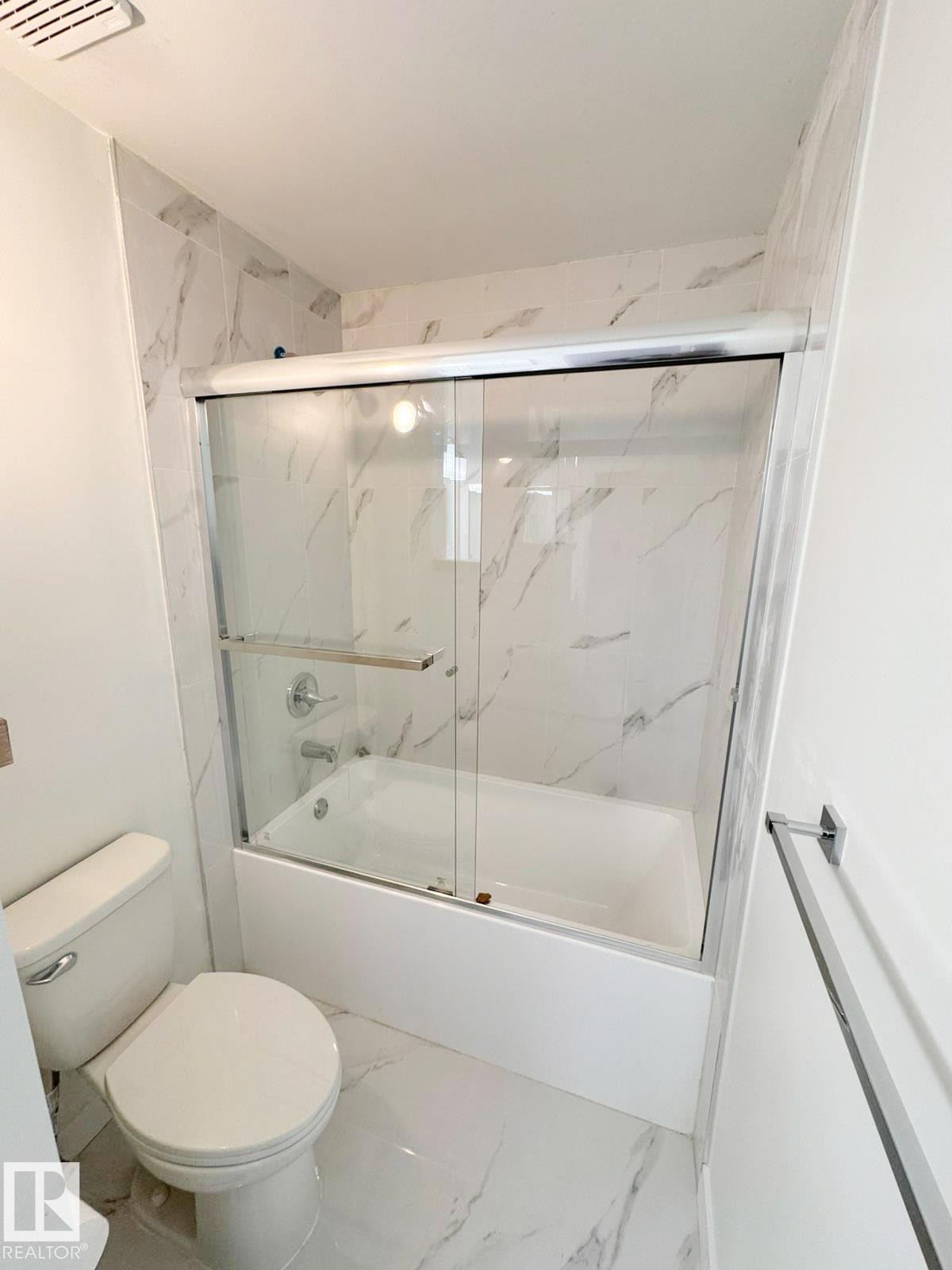 Bathroom featuring a white tub, sliding glass shower doors, a standard toilet, and marbled tile flooring and walls - 20 Hunt Road, Edmonton, AB - Indoor Photo Showing Bathroom