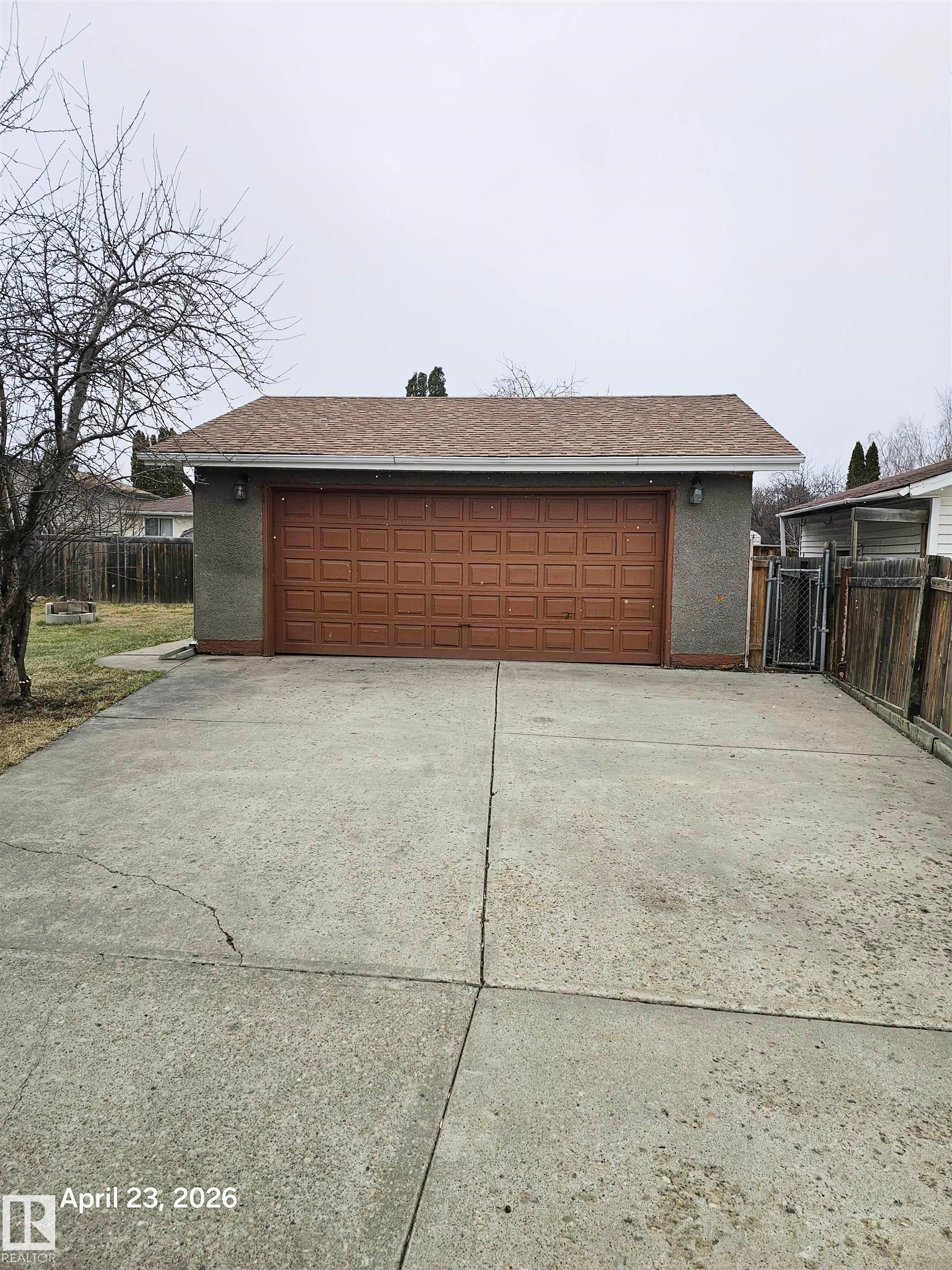 Detached garage with a brown panel door, grey stucco exterior, and asphalt shingle roof - 20 Hunt Road, Edmonton, AB - Outdoor