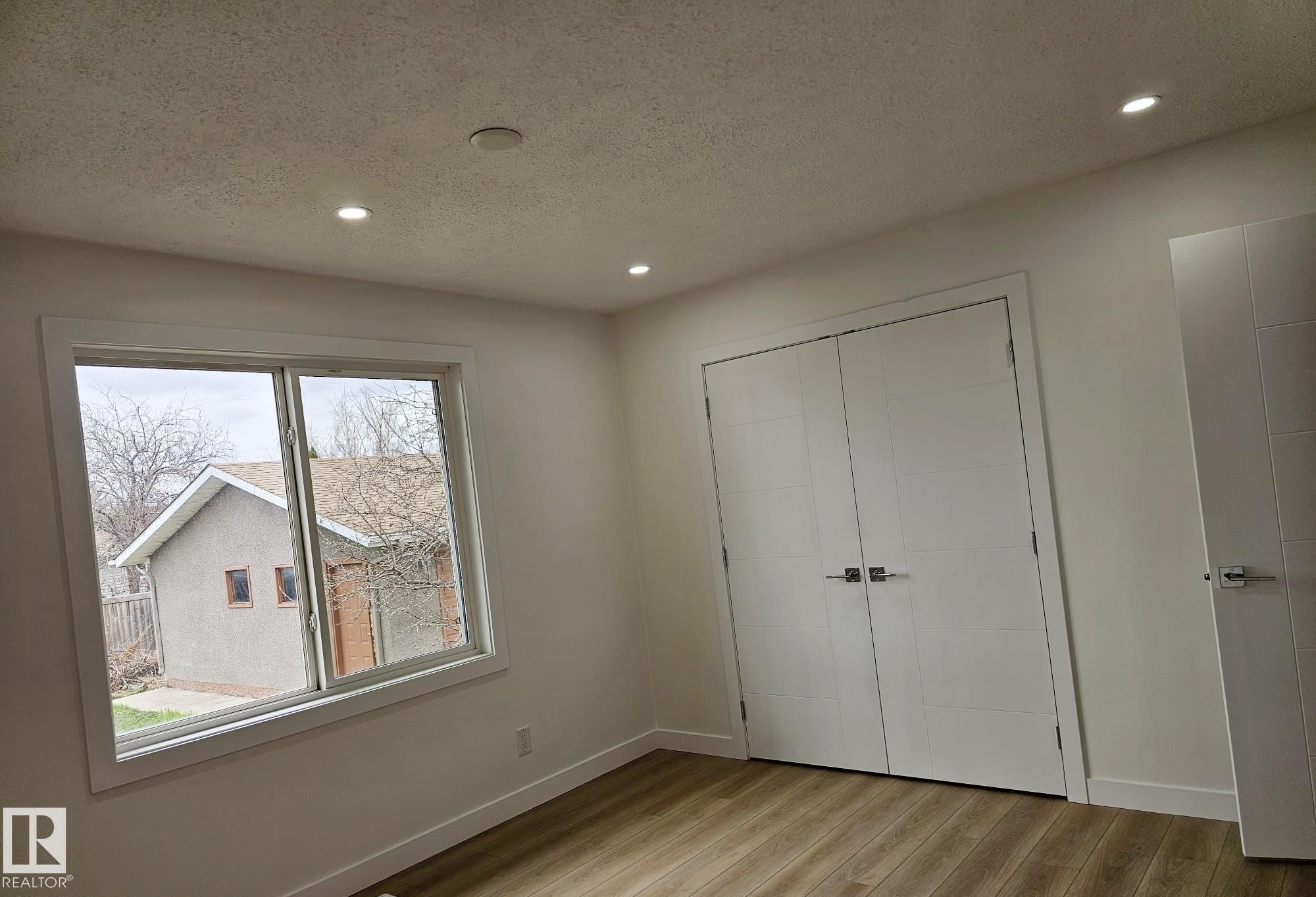 Bright interior space featuring a large window, recessed lighting, wood-finish flooring, and a double bi-fold closet with contemporary hardware - 20 Hunt Road, Edmonton, AB - Indoor Photo Showing Other Room