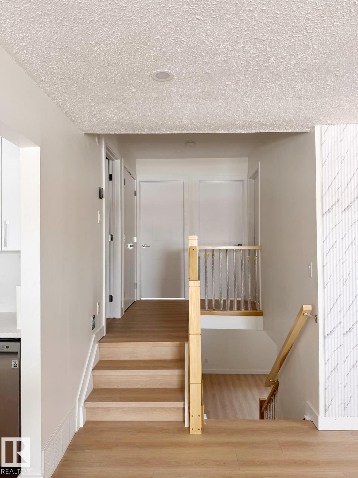 Hardwood stairs and wood-finish flooring with a white textured accent wall - 20 Hunt Road, Edmonton, AB - Indoor Photo Showing Other Room