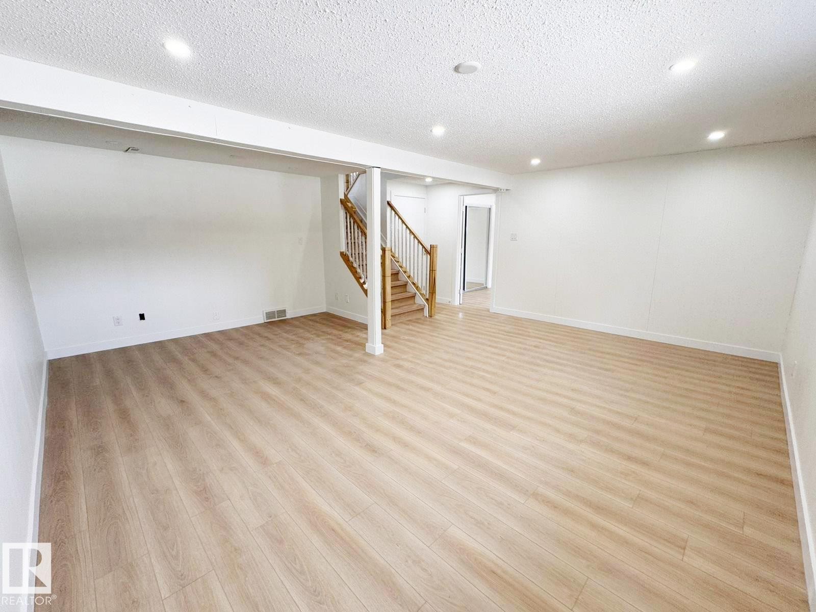 Spacious room featuring light wood-finish flooring, recessed ceiling lighting, and a prominent wood staircase with white risers and railings - 20 Hunt Road, Edmonton, AB - Indoor Photo Showing Other Room
