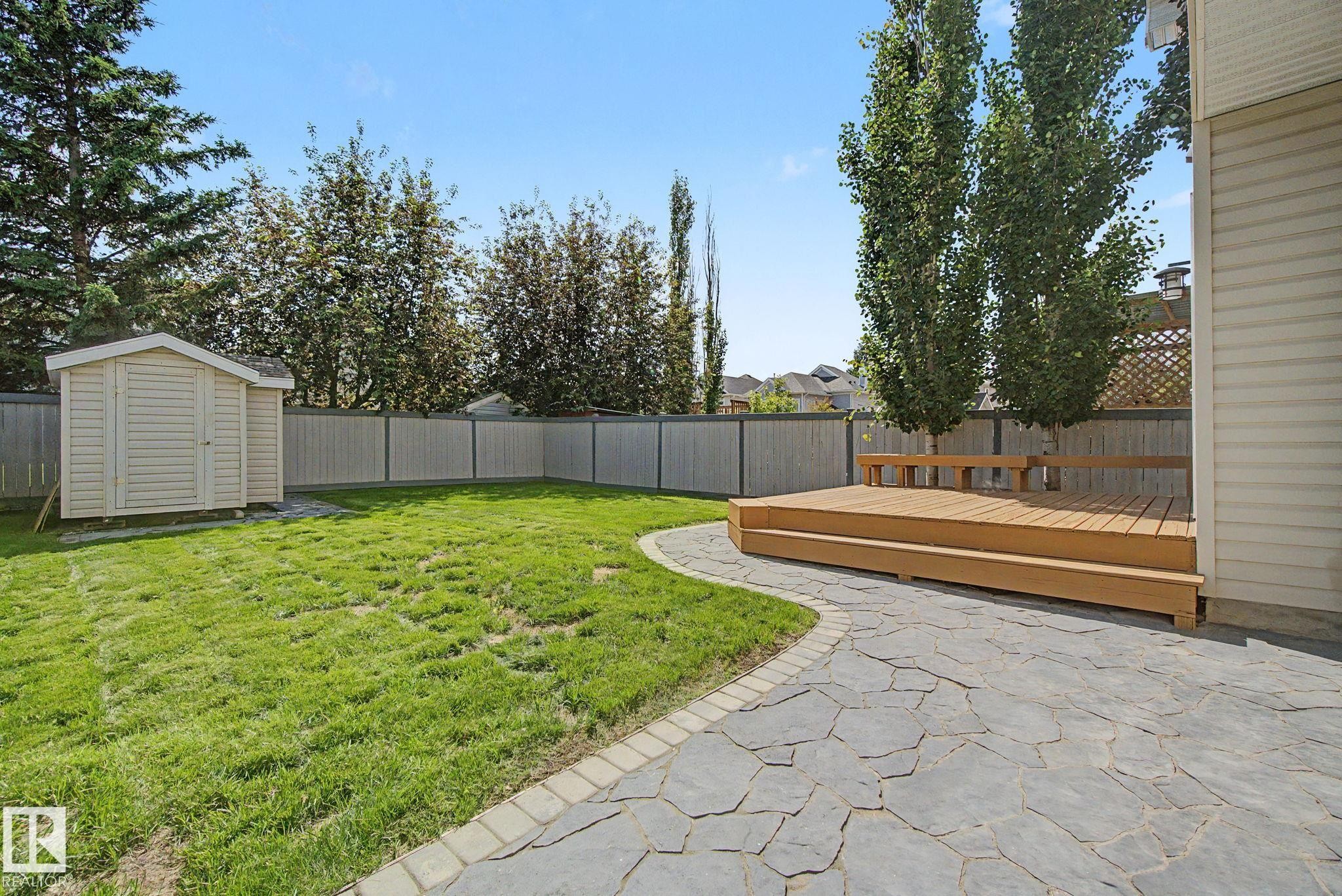 Expansive backyard featuring a wood deck with integrated seating, a flagstone patio, a manicured lawn, a detached storage shed, and a privacy fence - 8311 11 Avenue, Edmonton, AB