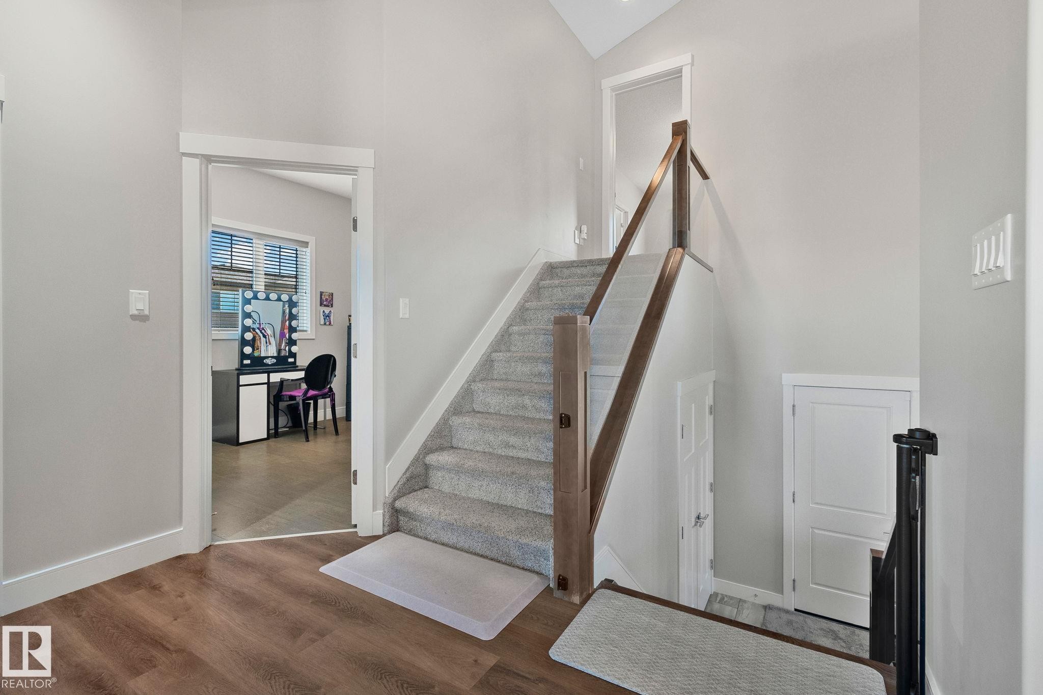 Carpeted staircase featuring a wood and glass railing, wood-finish flooring, and white trim throughout - 67 Enchanted Way Nw, St. Albert, AB - Indoor Photo Showing Other Room