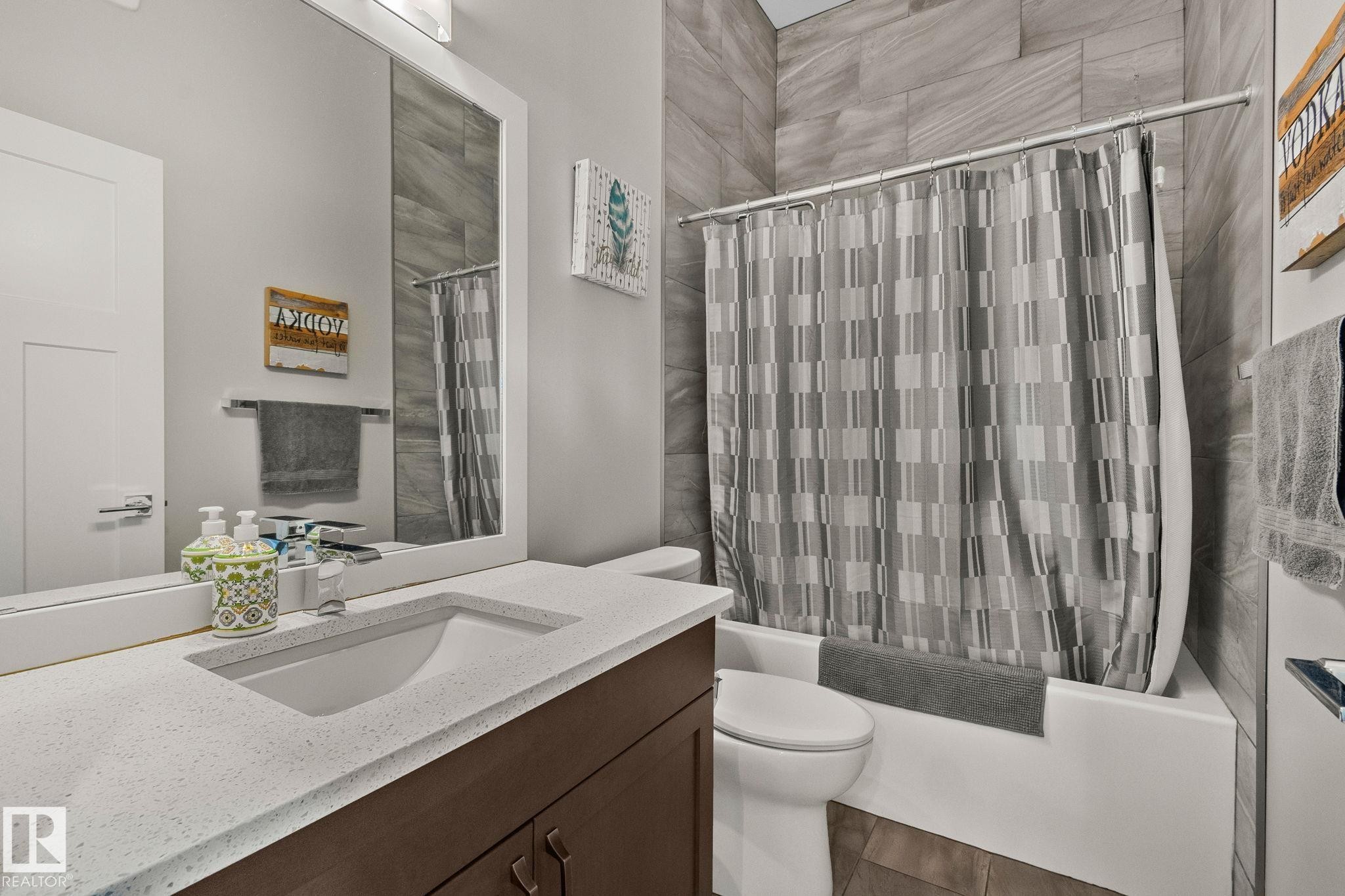 Bathroom featuring a white framed mirror, a vanity with a white speckled countertop, a rectangular undermount sink, a dark wood-finish cabinet, and a white bathtub with a gray tiled surround - 67 Enchanted Way Nw, St. Albert, AB - Indoor Photo Showing Bathroom