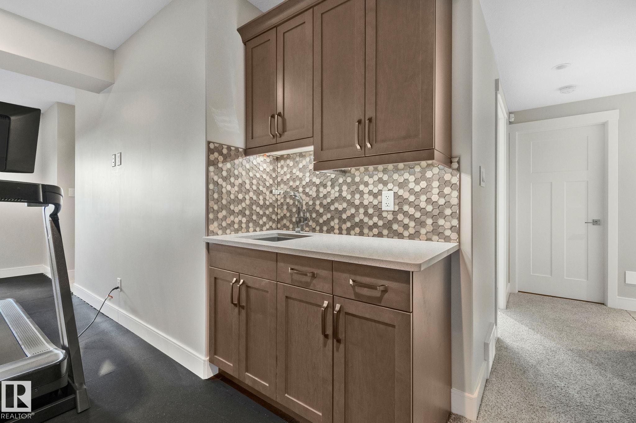 Built-in wet bar with wood cabinetry, light countertop, and a hexagonal tile backsplash - 67 Enchanted Way Nw, St. Albert, AB - Indoor Photo Showing Other Room