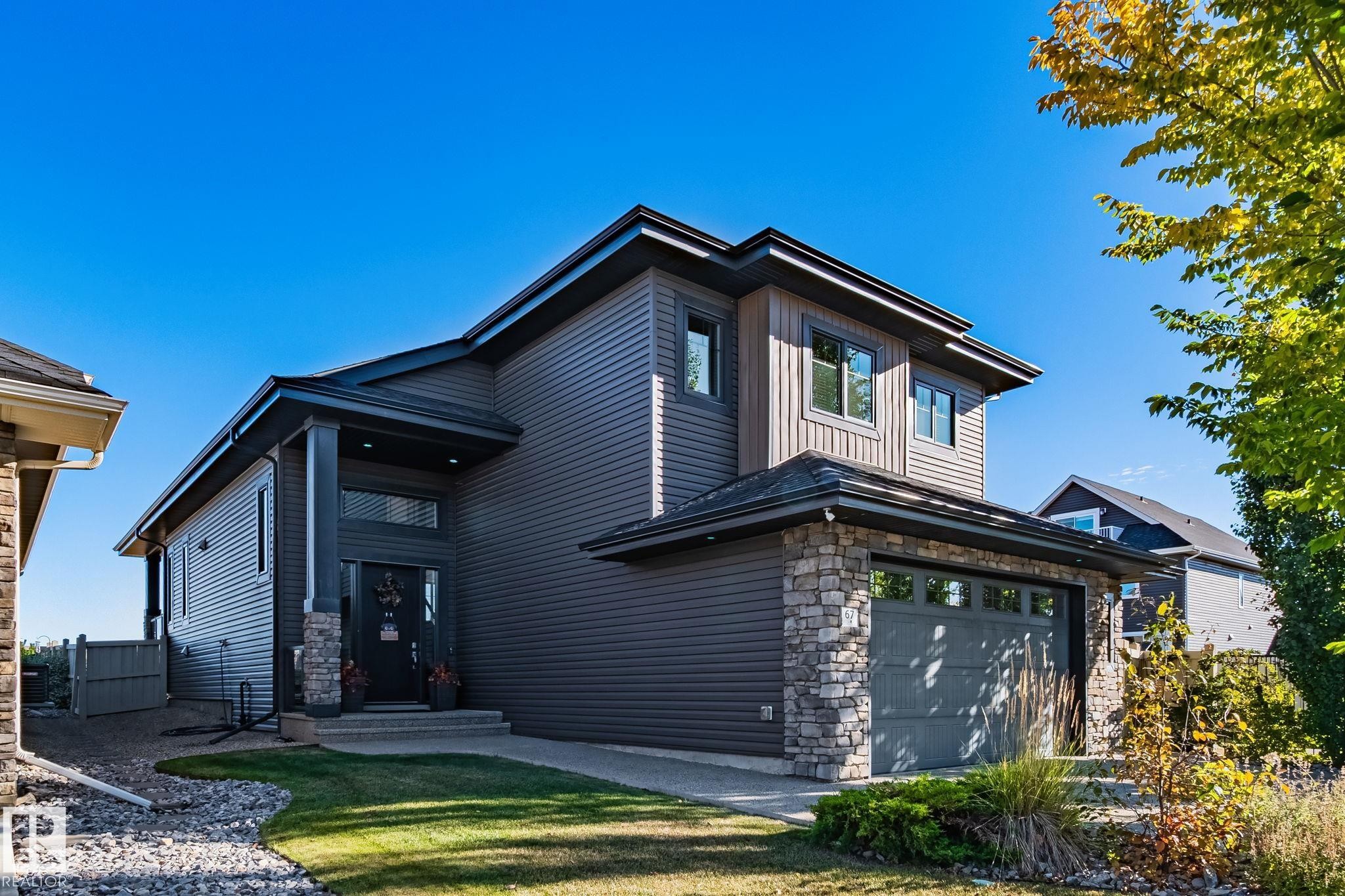 Contemporary exterior featuring dark horizontal siding, natural stone accents, a large attached garage, covered entryway, and second-story windows - 67 Enchanted Way Nw, St. Albert, AB - Outdoor