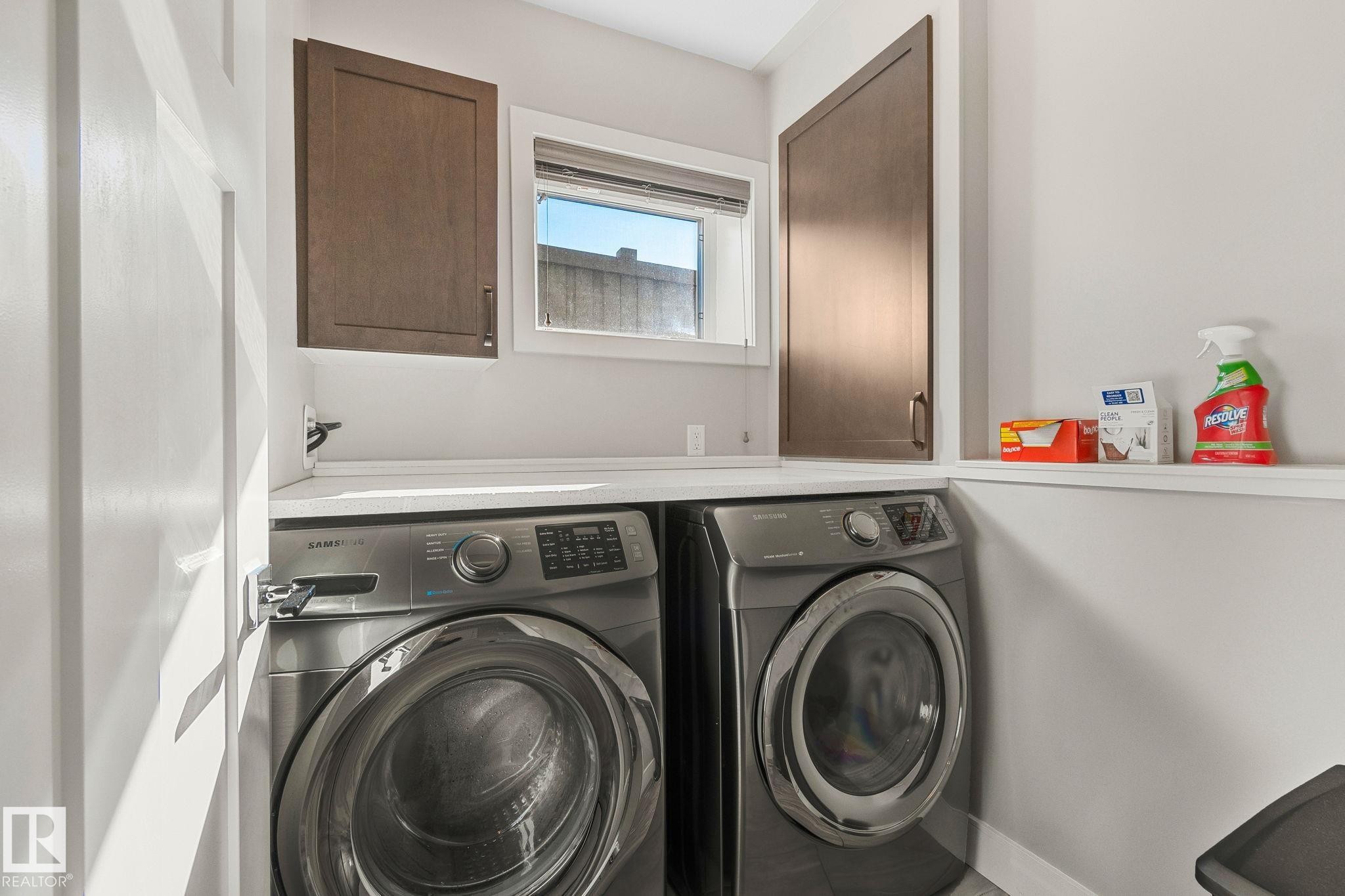 Dedicated laundry area featuring a white countertop, upper wood-finish cabinetry, built-in shelving, and a window for natural light - 67 Enchanted Way Nw, St. Albert, AB - Indoor Photo Showing Laundry Room