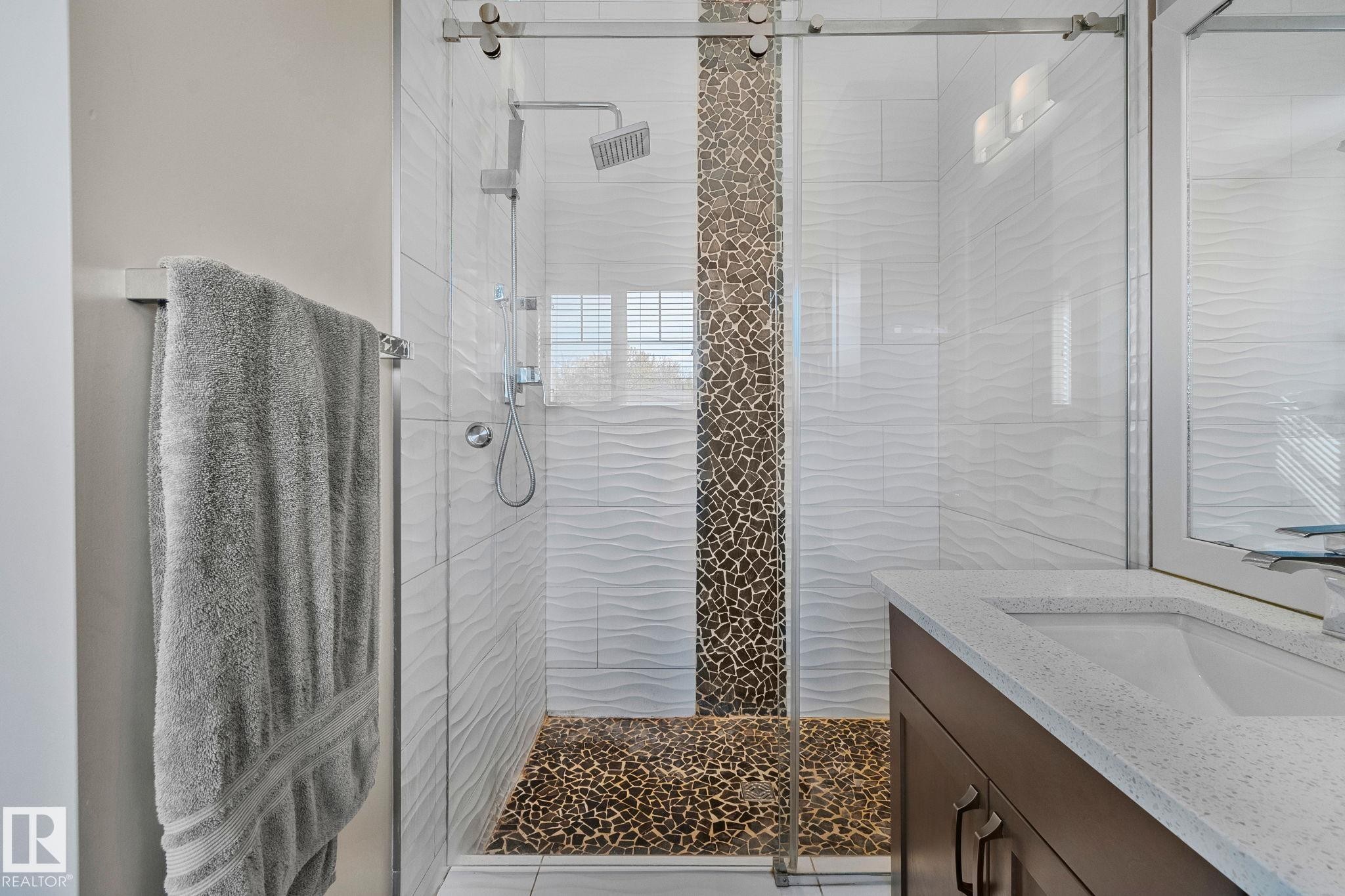 Glass-enclosed shower featuring a rain showerhead, mosaic pebble tile accent, and textured white subway tile - 67 Enchanted Way Nw, St. Albert, AB - Indoor Photo Showing Bathroom