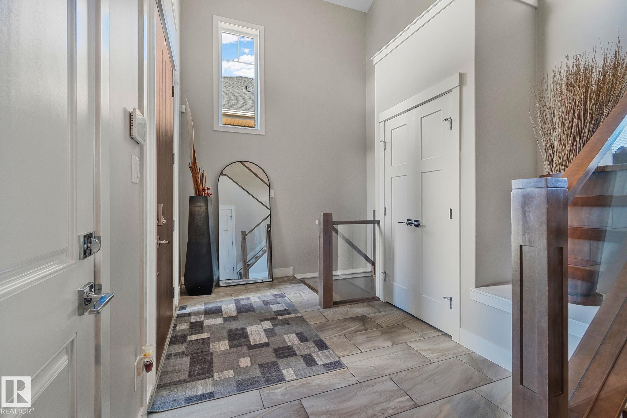 Entryway featuring tile flooring, a high ceiling, and a prominent staircase with wood newel posts and glass panels - 67 Enchanted Way Nw, St. Albert, AB - Indoor Photo Showing Other Room