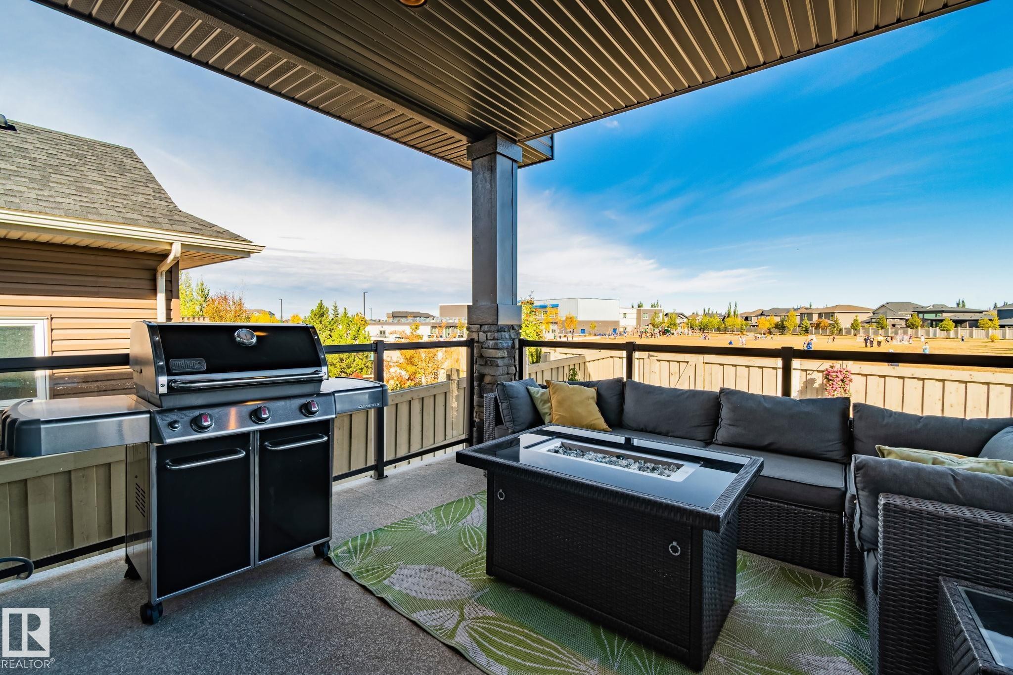 Covered outdoor patio featuring a built-in outdoor kitchen, stone pillar accents, and a glass panel railing - 67 Enchanted Way Nw, St. Albert, AB - Outdoor With Deck Patio Veranda With Exterior