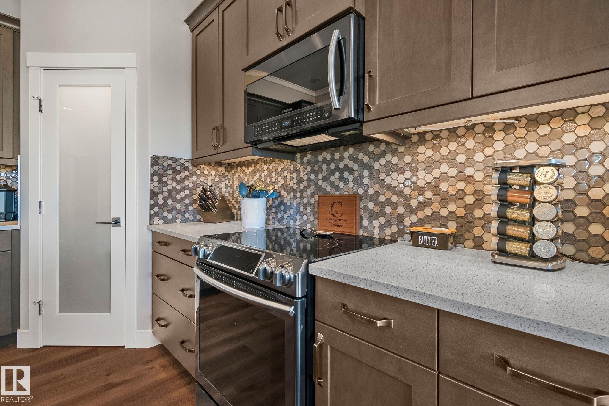 Kitchen featuring warm wood-finish cabinetry and a complementary hexagonal tile backsplash - 67 Enchanted Way Nw, St. Albert, AB - Indoor Photo Showing Kitchen