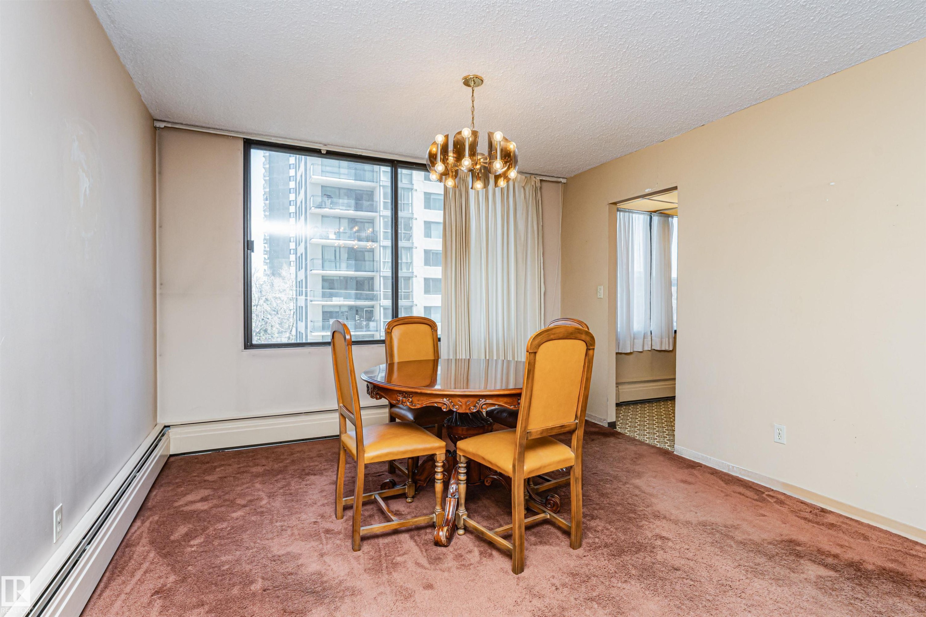 Dining area featuring a large window, textured ceiling, brown carpeting, and a built-in baseboard heater - 407 10045 118 Street, Edmonton, AB - Indoor Photo Showing Dining Room