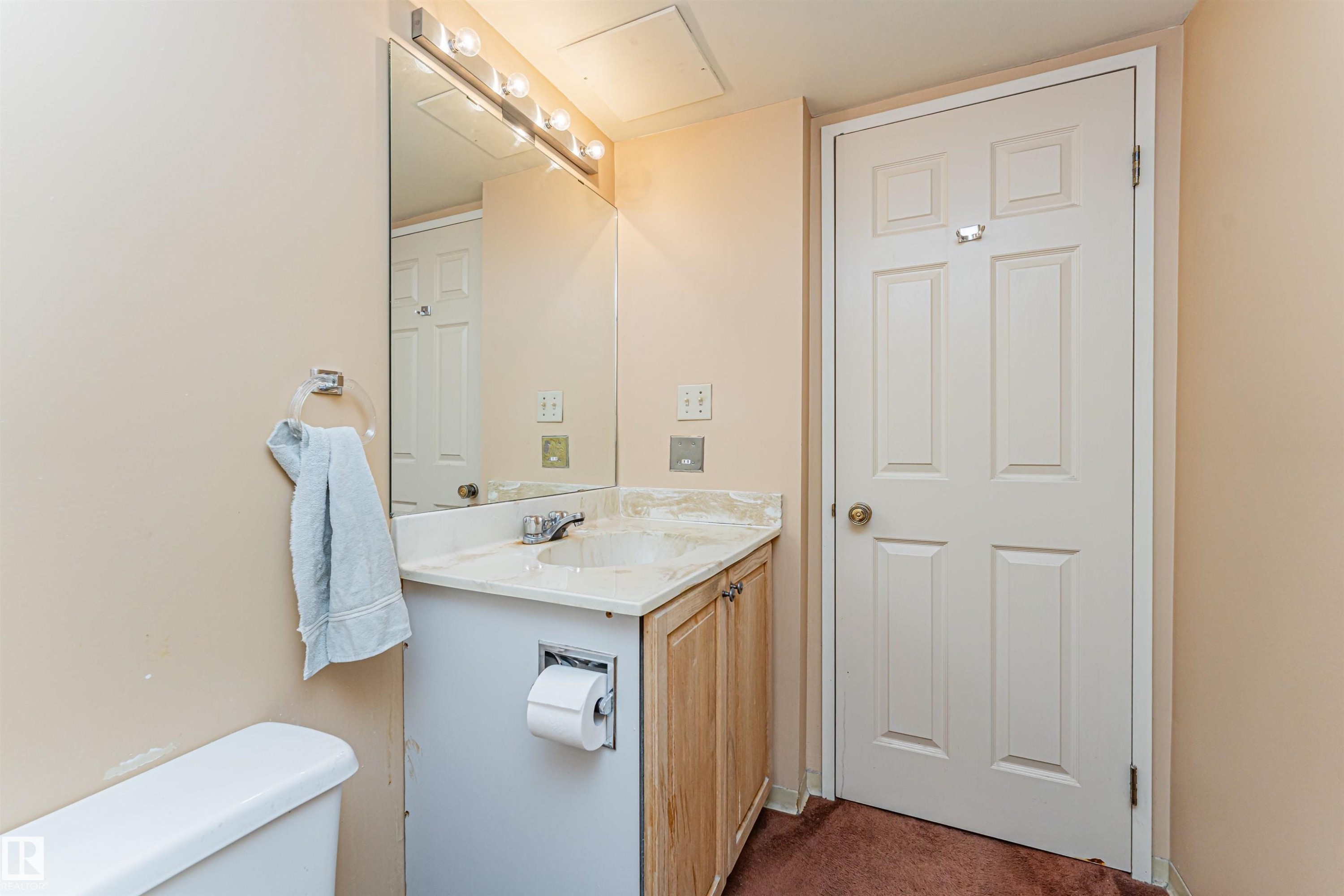 Bathroom vanity featuring a single sink, light-toned countertop, wood-finish cabinetry, and an overhead light bar - 407 10045 118 Street, Edmonton, AB - Indoor Photo Showing Bathroom