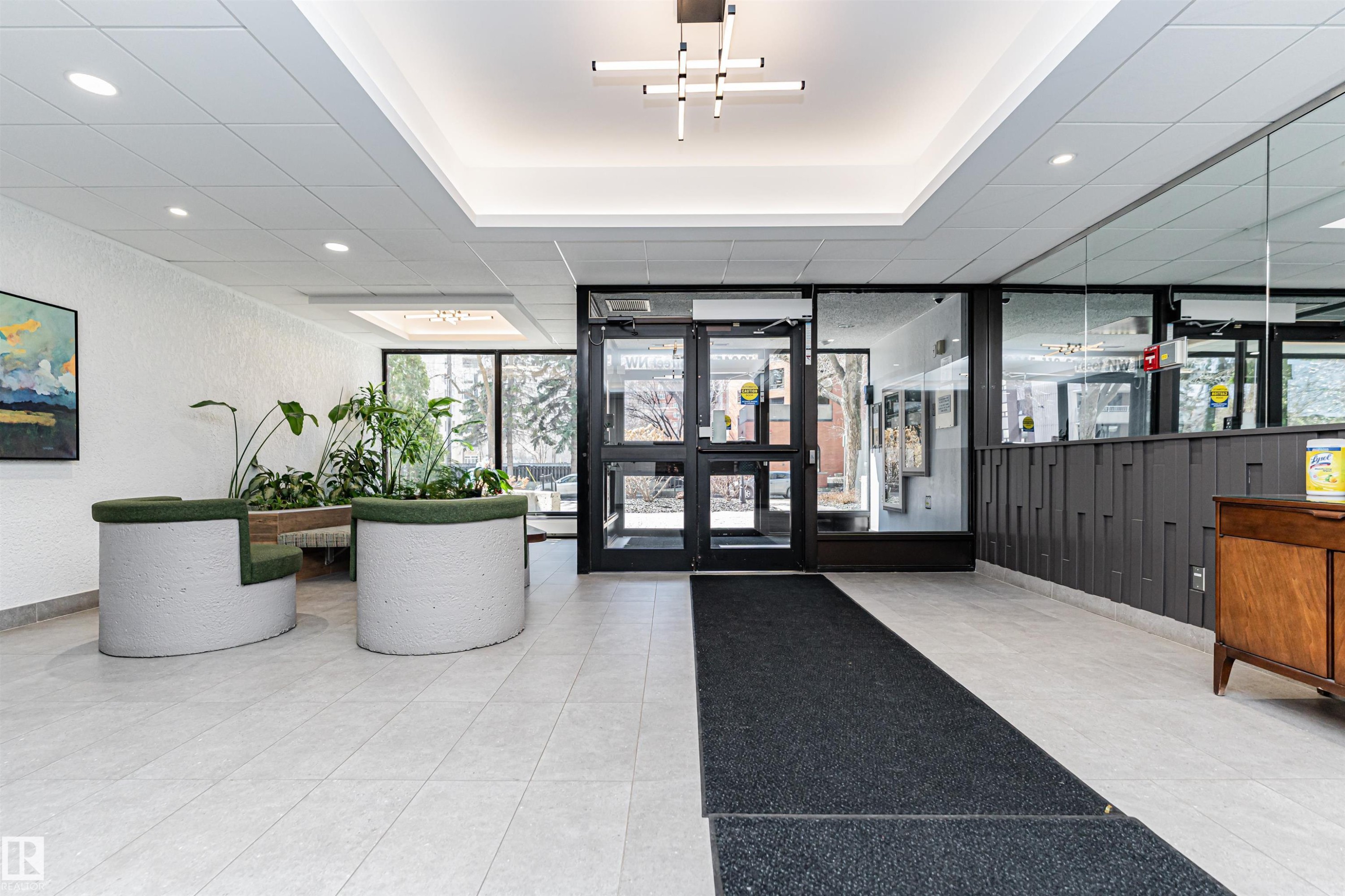 Spacious lobby featuring light-toned tile flooring, recessed lighting, and a modern linear chandelier - 407 10045 118 Street, Edmonton, AB - Indoor Photo Showing Other Room