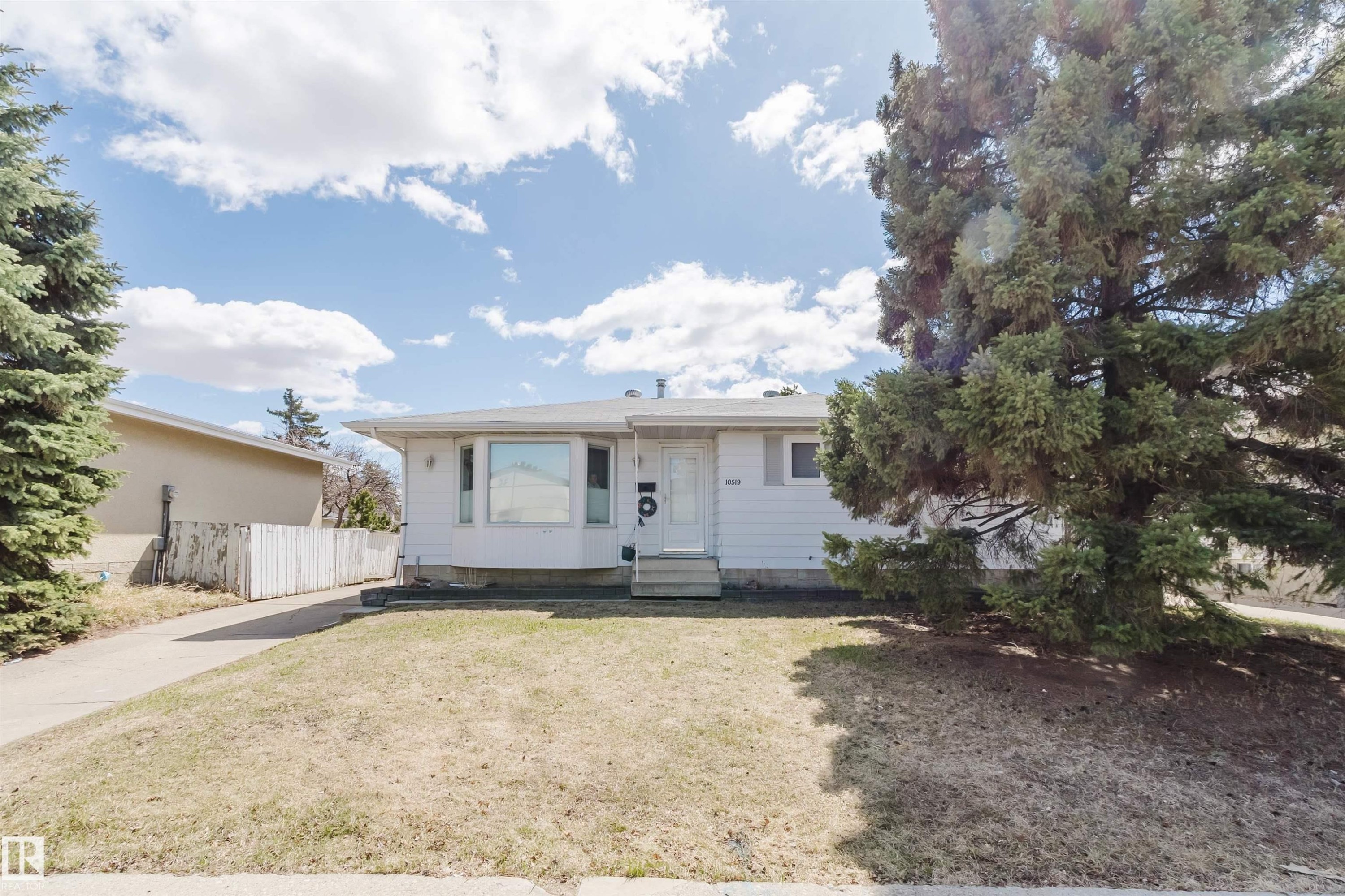 White single-story residence featuring a bay window, concrete driveway, and mature evergreen landscaping - 10519 36A Avenue, Edmonton, AB - Outdoor