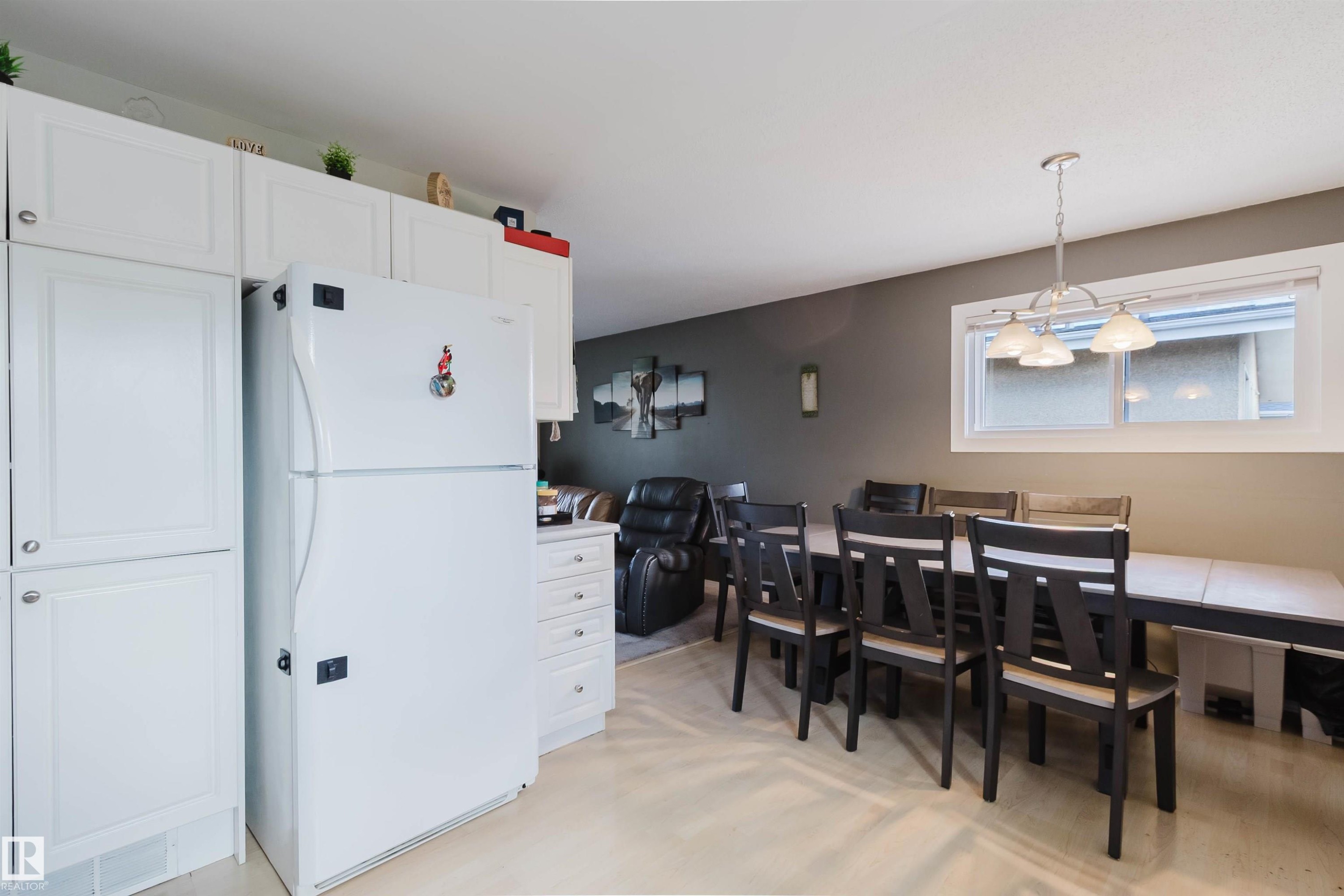 Open-concept kitchen and dining area featuring white cabinetry, a white refrigerator, and a dining space with a pendant light fixture - 10519 36A Avenue, Edmonton, AB - Indoor Photo Showing Dining Room