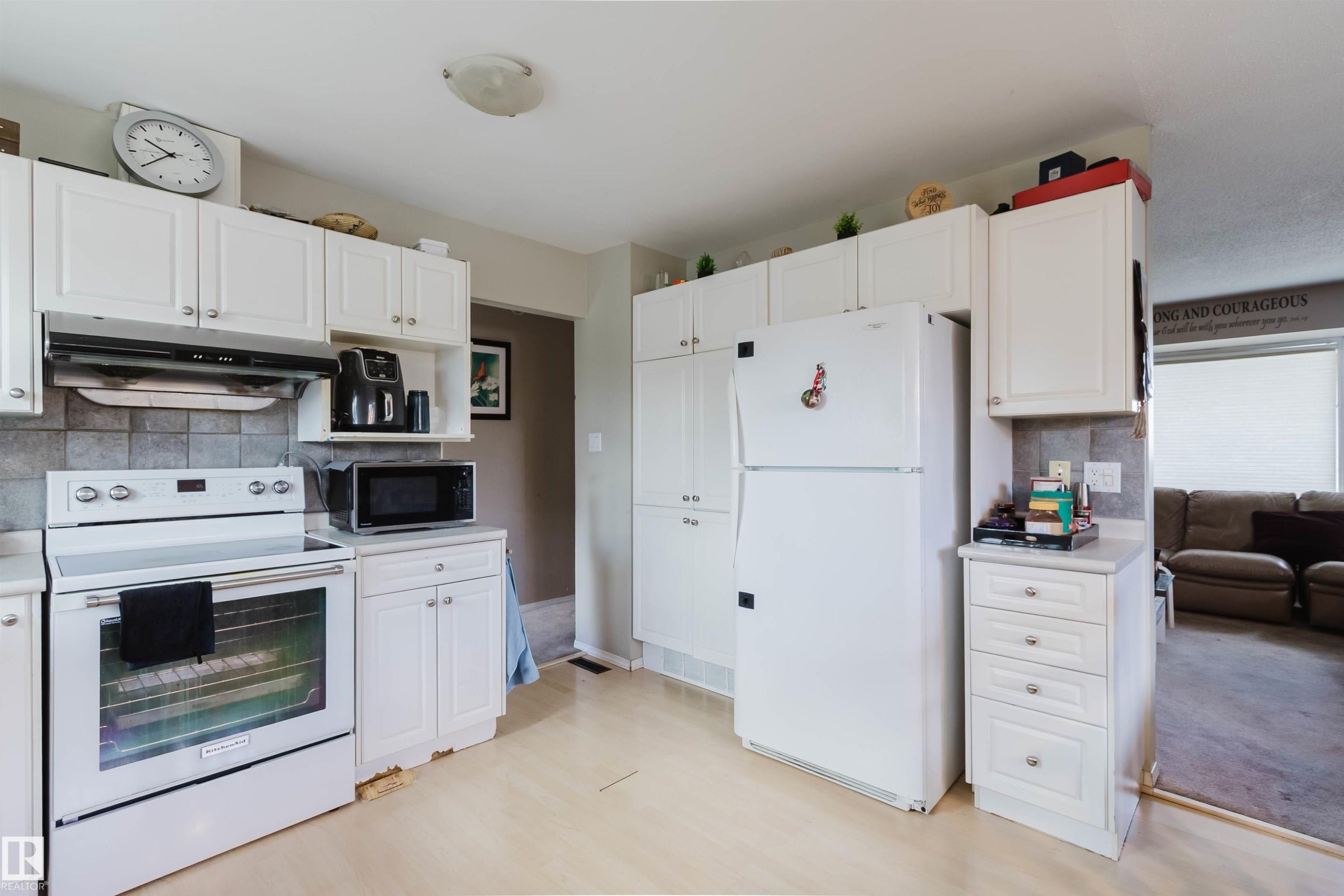 Kitchen featuring white cabinetry, tile backsplash, white appliances, and wood-finish flooring - 10519 36A Avenue, Edmonton, AB - Indoor Photo Showing Kitchen