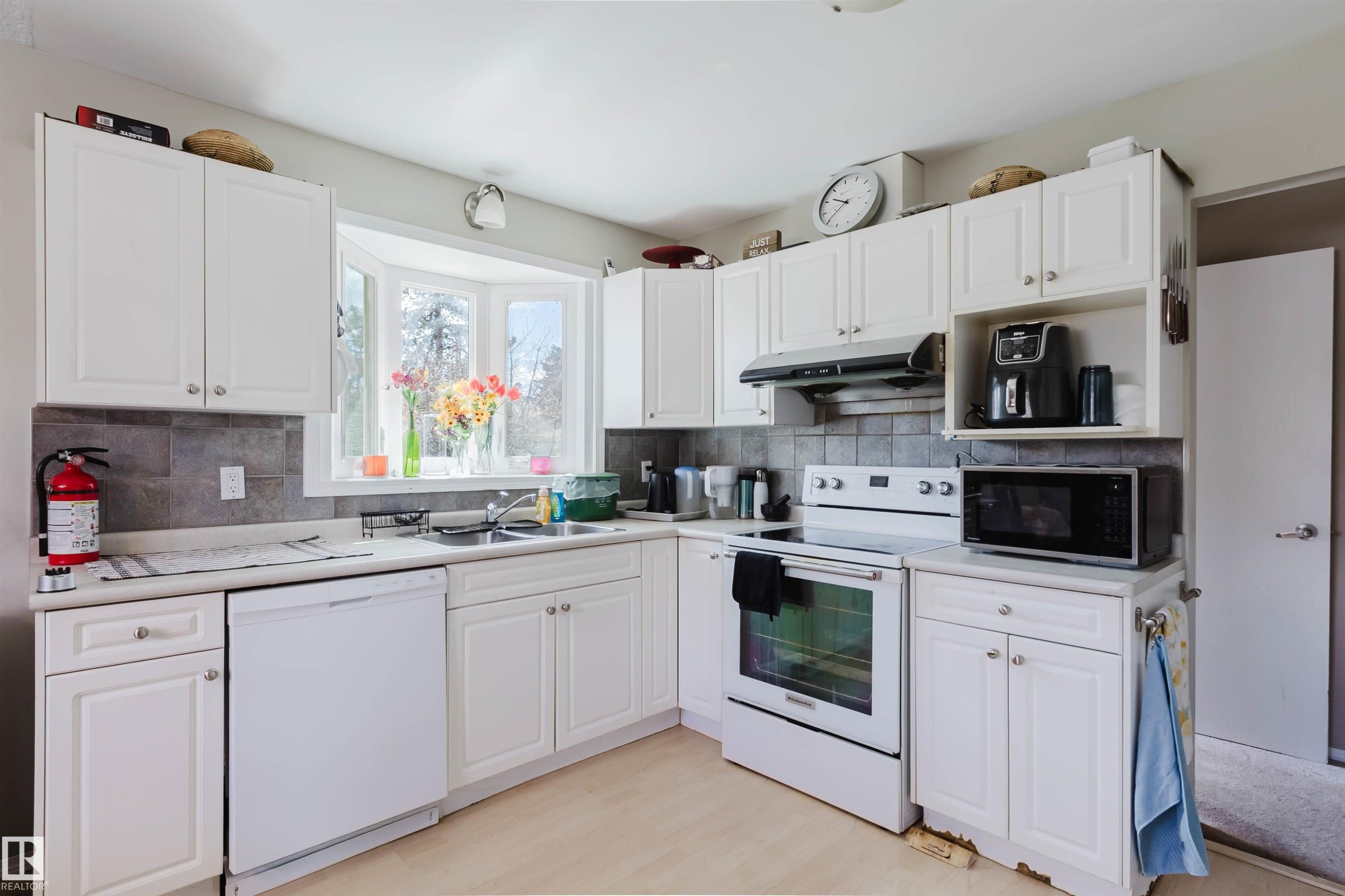 Kitchen featuring white cabinetry, a bay window, tile backsplash, laminate countertops, and wood-finish flooring - 10519 36A Avenue, Edmonton, AB - Indoor Photo Showing Kitchen With Double Sink