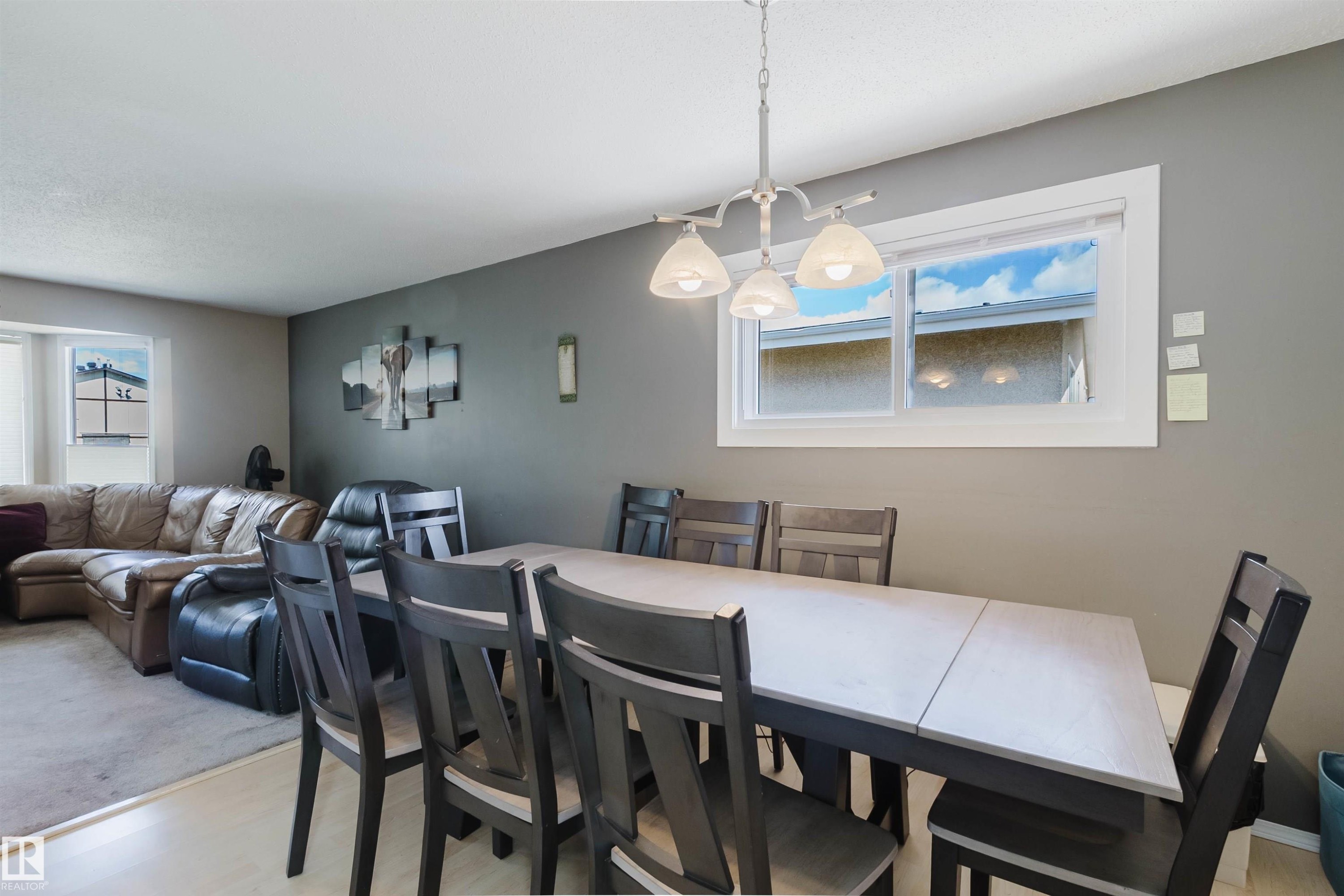 Dining area with wood-finish flooring, a white-framed window, and a chandelier featuring three bell-shaped lights - 10519 36A Avenue, Edmonton, AB - Indoor Photo Showing Dining Room