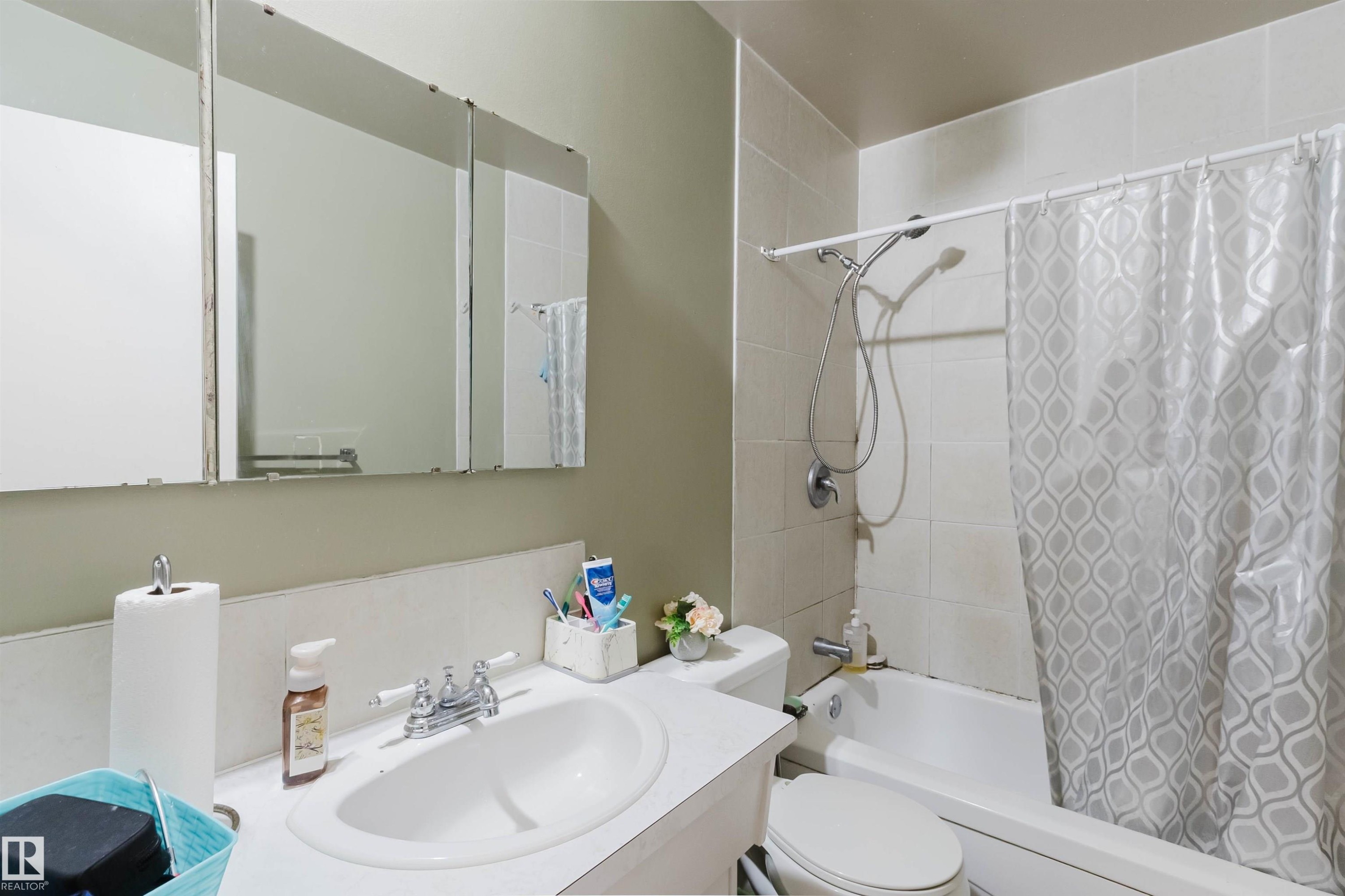 Bathroom featuring a vanity with an integrated sink, a three-panel mirrored medicine cabinet, and a white tiled shower/tub combination with a shower head and handheld spray - 10519 36A Avenue, Edmonton, AB - Indoor Photo Showing Bathroom