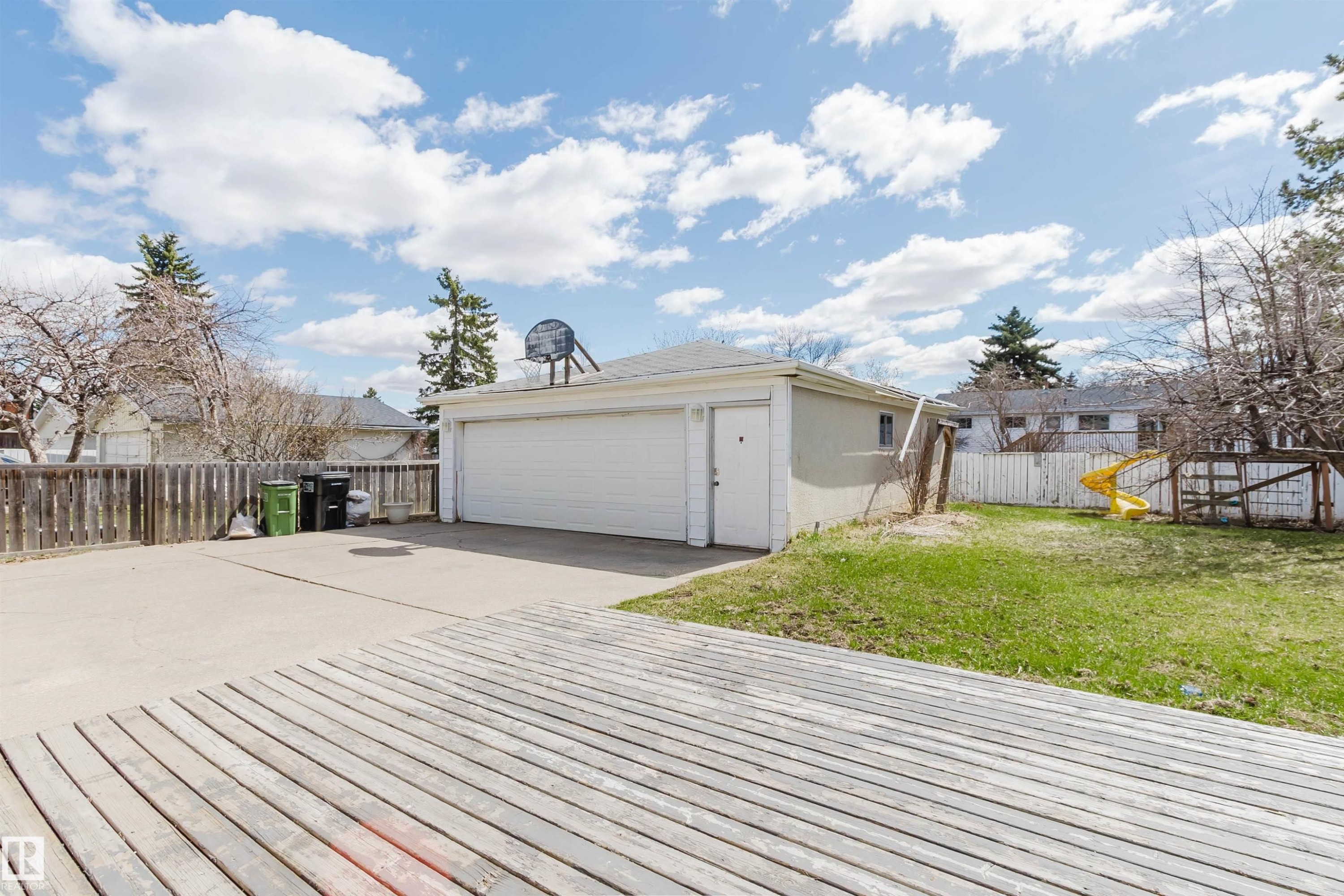 Expansive backyard featuring a concrete patio, wooden deck, and a detached garage with a white overhead door - 10519 36A Avenue, Edmonton, AB - Outdoor