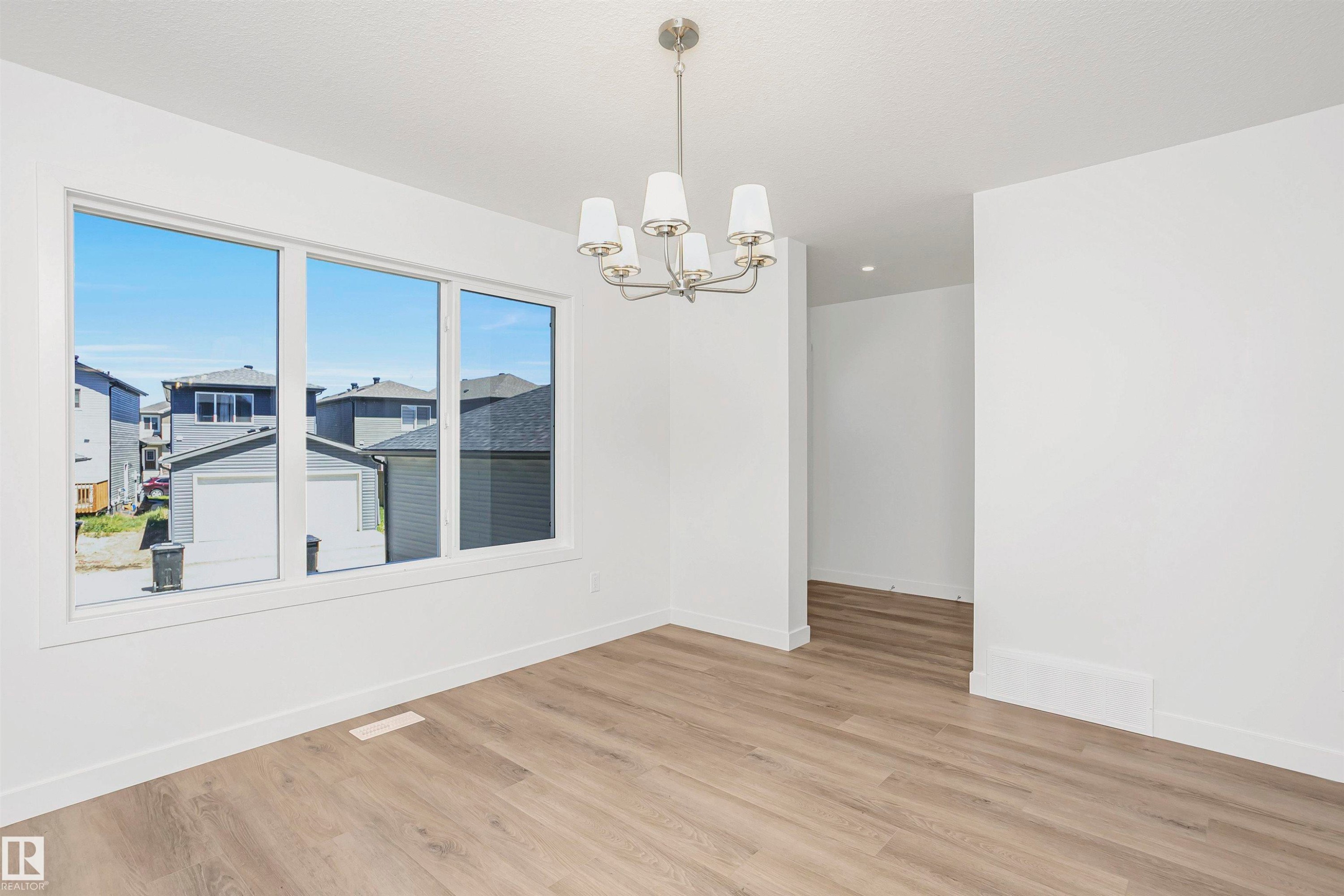 Spacious room featuring light wood-finish flooring, a contemporary chandelier, white walls, and a large triple window - 9552 Carson Bend Bend, Edmonton, AB - Indoor Photo Showing Other Room