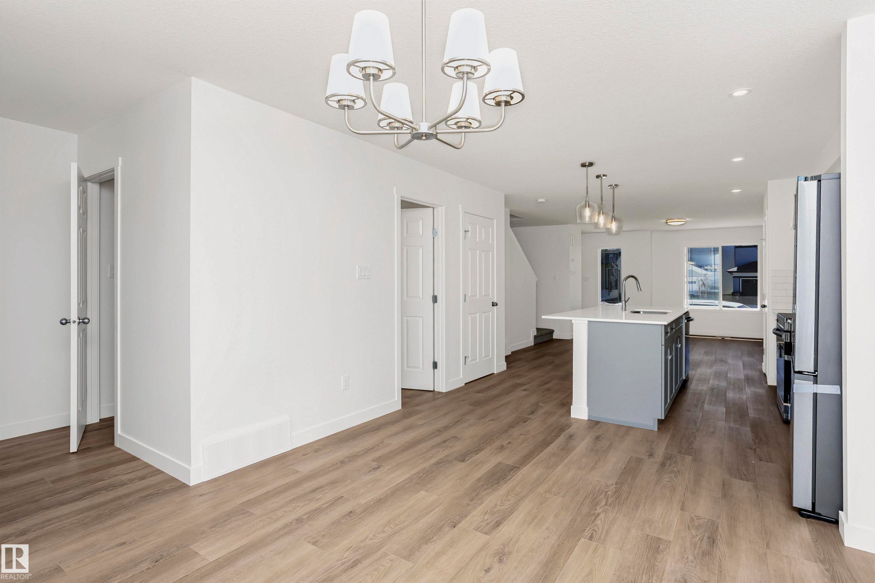Open-concept living area featuring wood-finish flooring, a modern chandelier, and a kitchen island with pendant lighting - 9552 Carson Bend Bend, Edmonton, AB - Indoor Photo Showing Kitchen