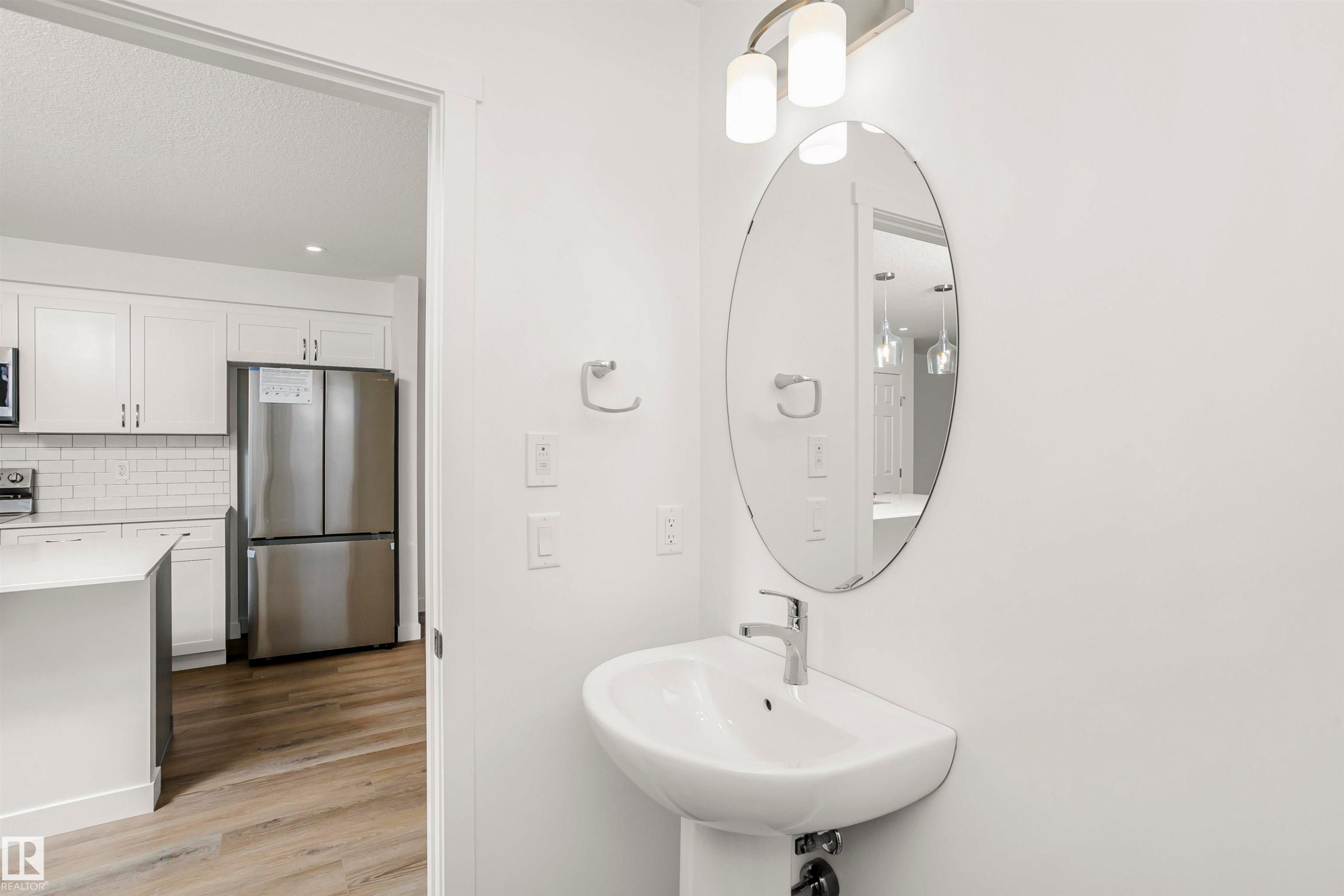 Pedestal sink with chrome faucet and oval mirror, complemented by an overhead two-light fixture - 9552 Carson Bend Bend, Edmonton, AB - Indoor Photo Showing Other Room