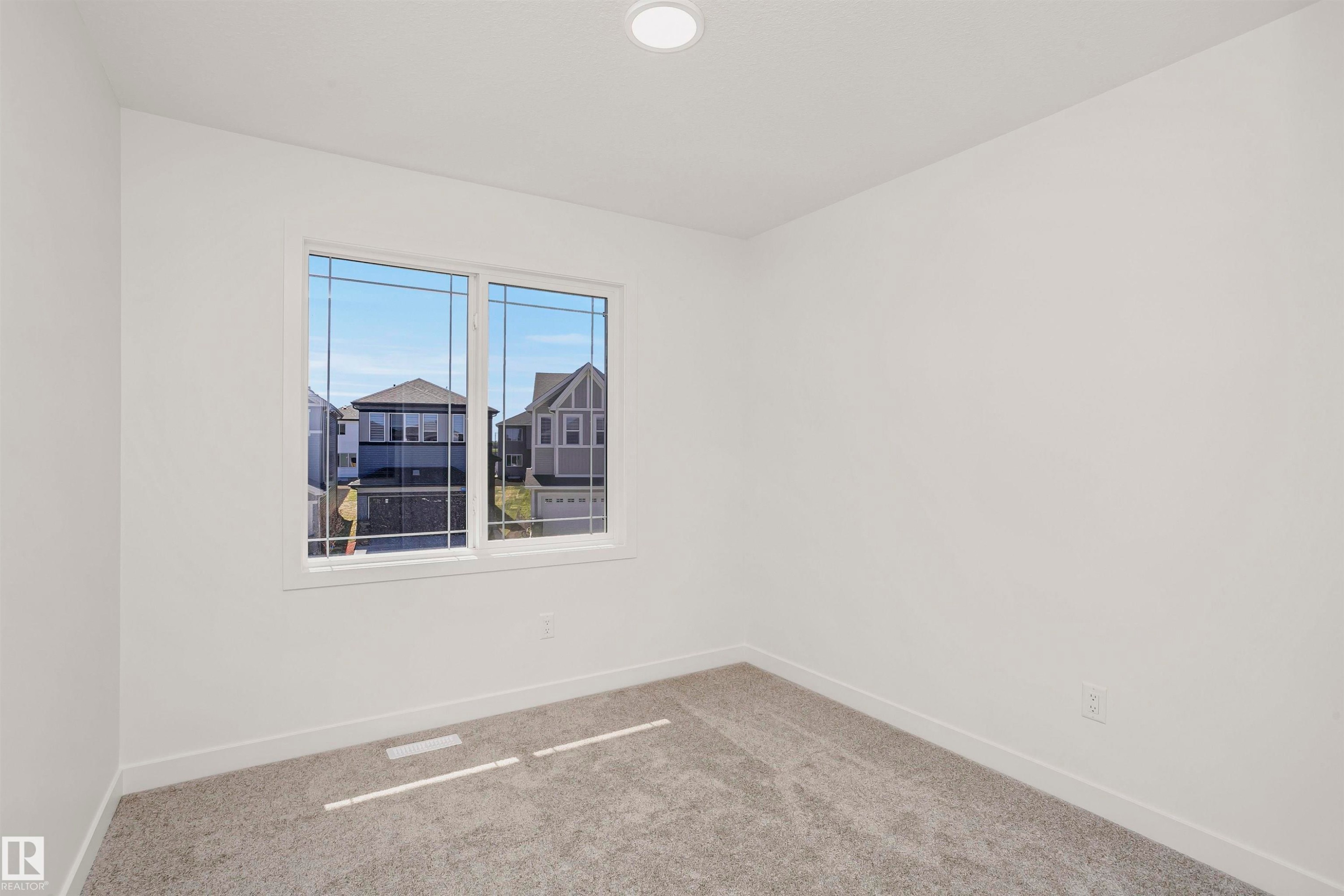 Bright interior space featuring a double window with grid patterns, recessed ceiling lighting, light gray carpet, and white baseboards - 9552 Carson Bend Bend, Edmonton, AB - Indoor Photo Showing Other Room