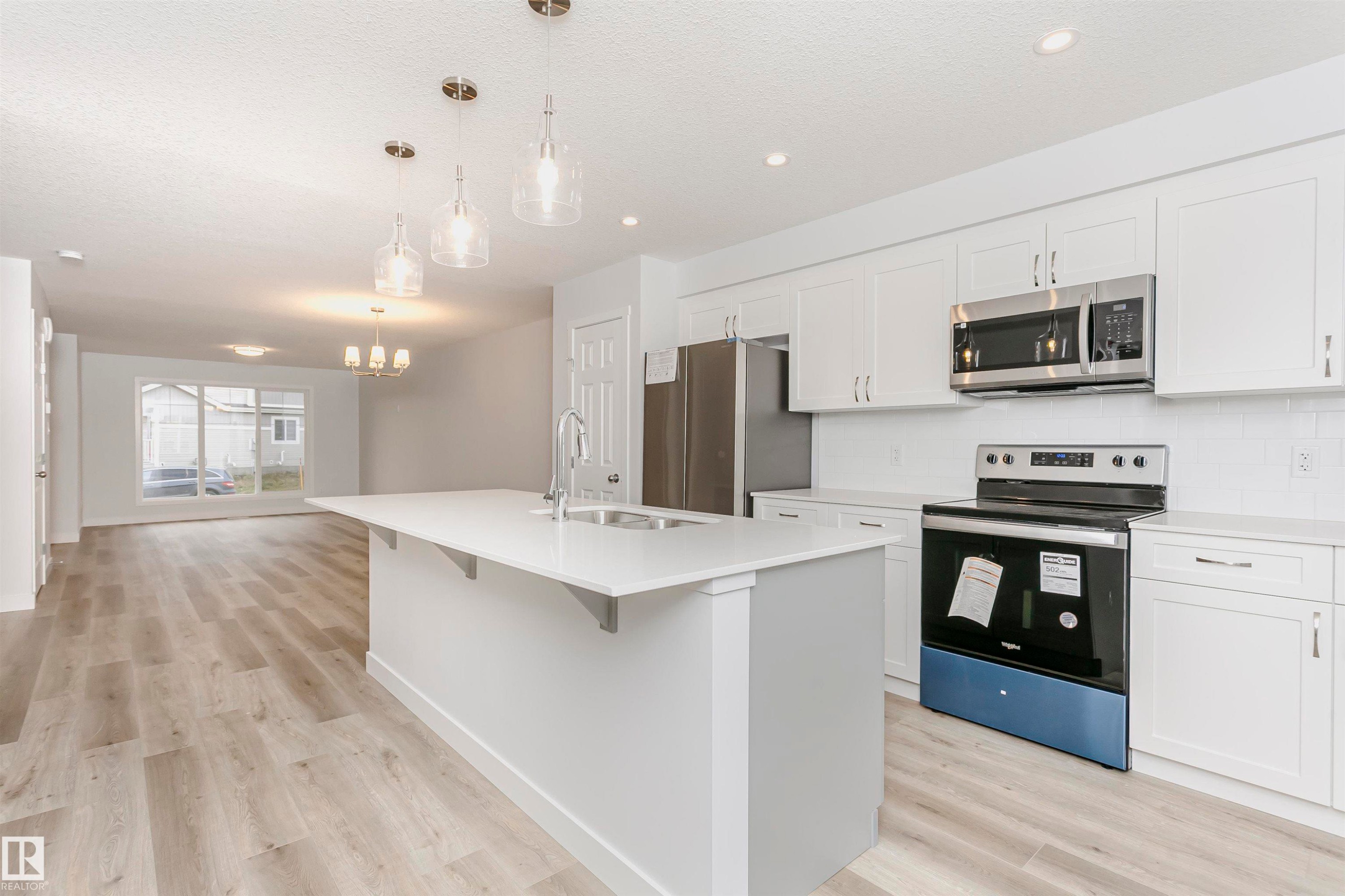 Kitchen featuring an island with sink, white cabinetry, stainless steel appliances, and wood-finish flooring - 9564 Carson Bend Bend, Edmonton, AB - Indoor Photo Showing Kitchen With Upgraded Kitchen