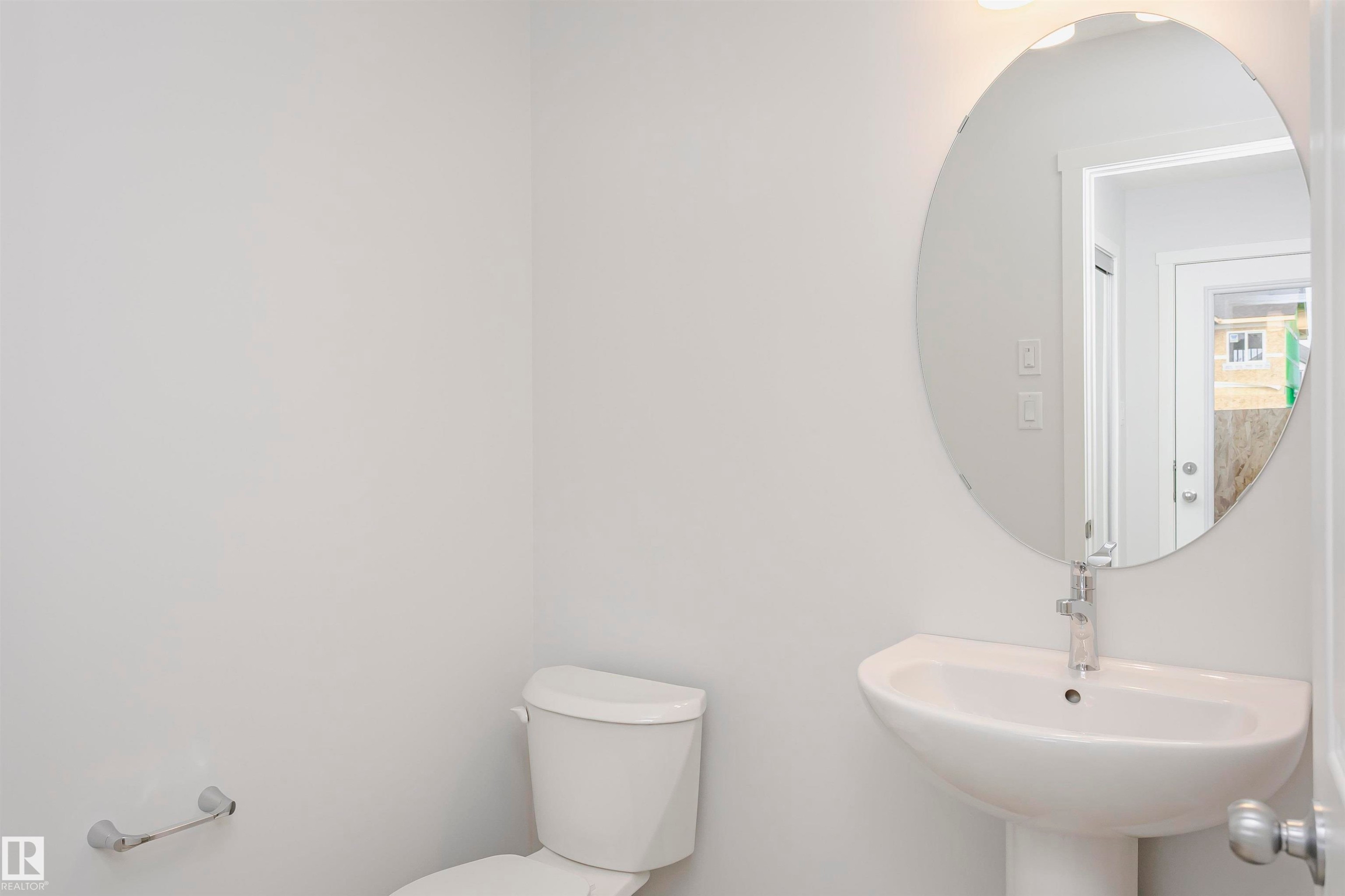 Bathroom featuring a pedestal sink with a chrome faucet, oval mirror, and white toilet - 9564 Carson Bend Bend, Edmonton, AB - Indoor Photo Showing Bathroom