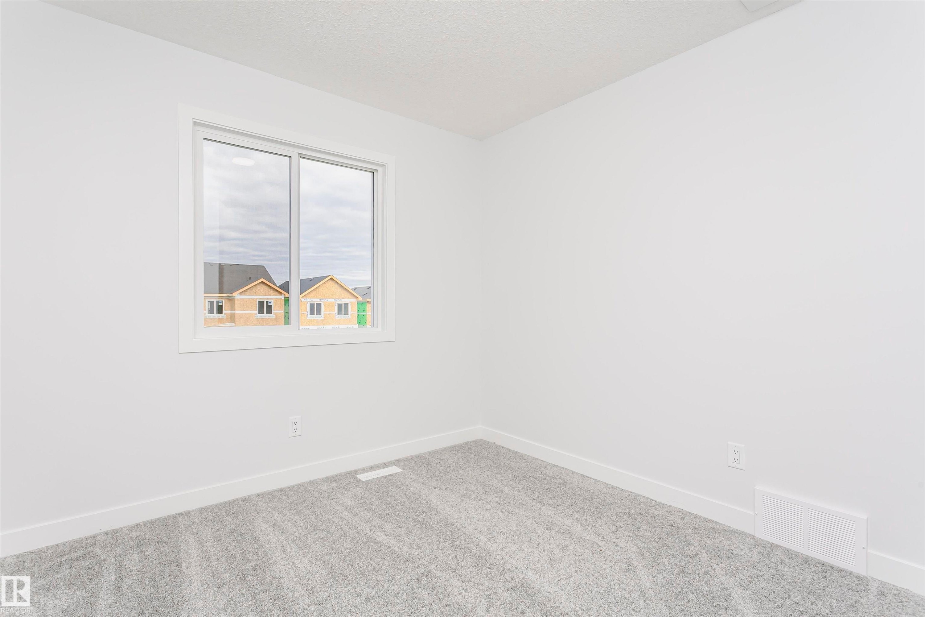 Bright interior space featuring a window with white trim, light gray patterned carpeting, white baseboards, and neutral wall tones - 9564 Carson Bend Bend, Edmonton, AB - Indoor Photo Showing Other Room