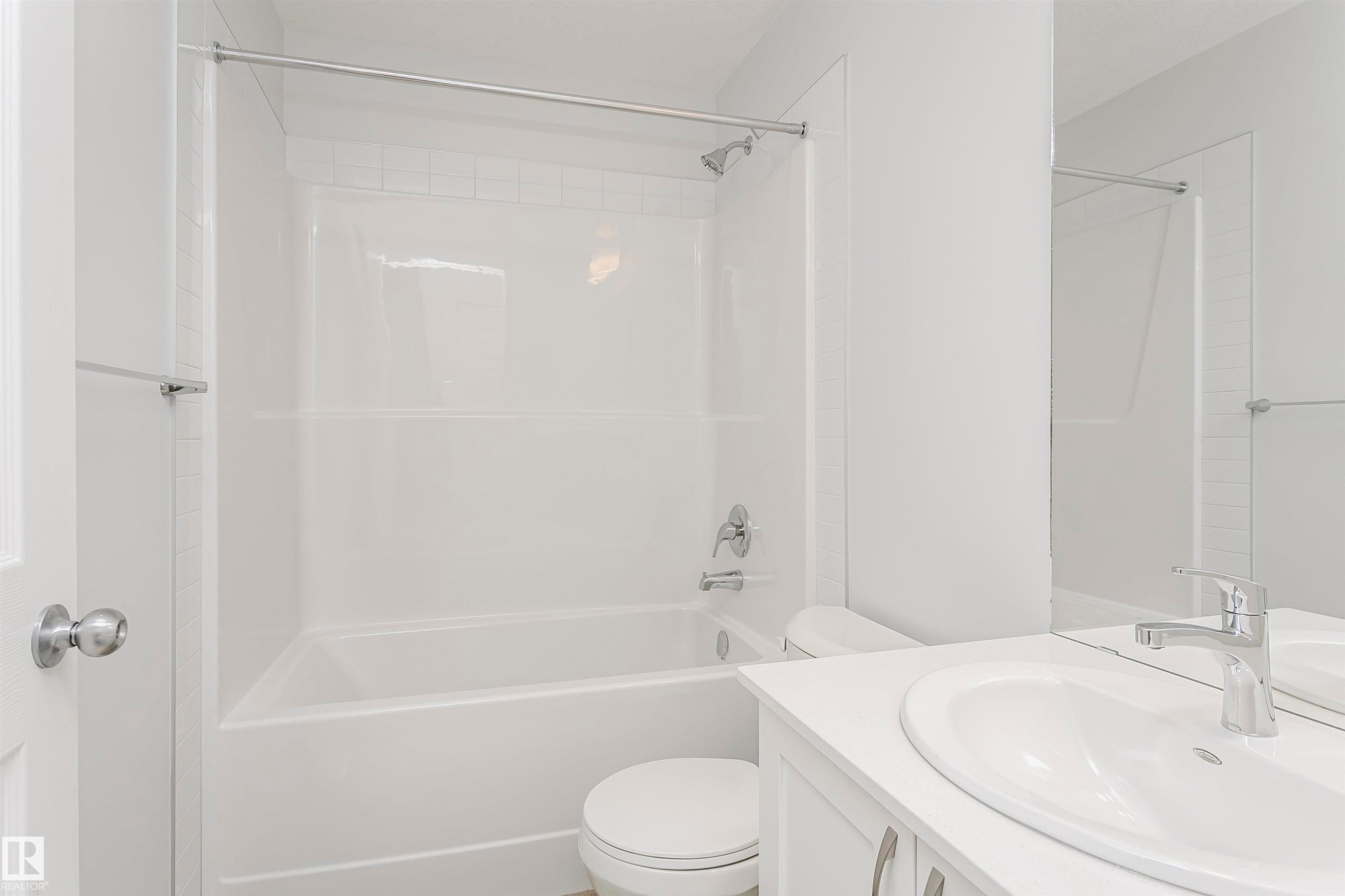 Bathroom featuring a bright white tub and shower combination with chrome fixtures, a white vanity with an integrated sink, a large mirror, and a modern toilet - 9564 Carson Bend Bend, Edmonton, AB - Indoor Photo Showing Bathroom