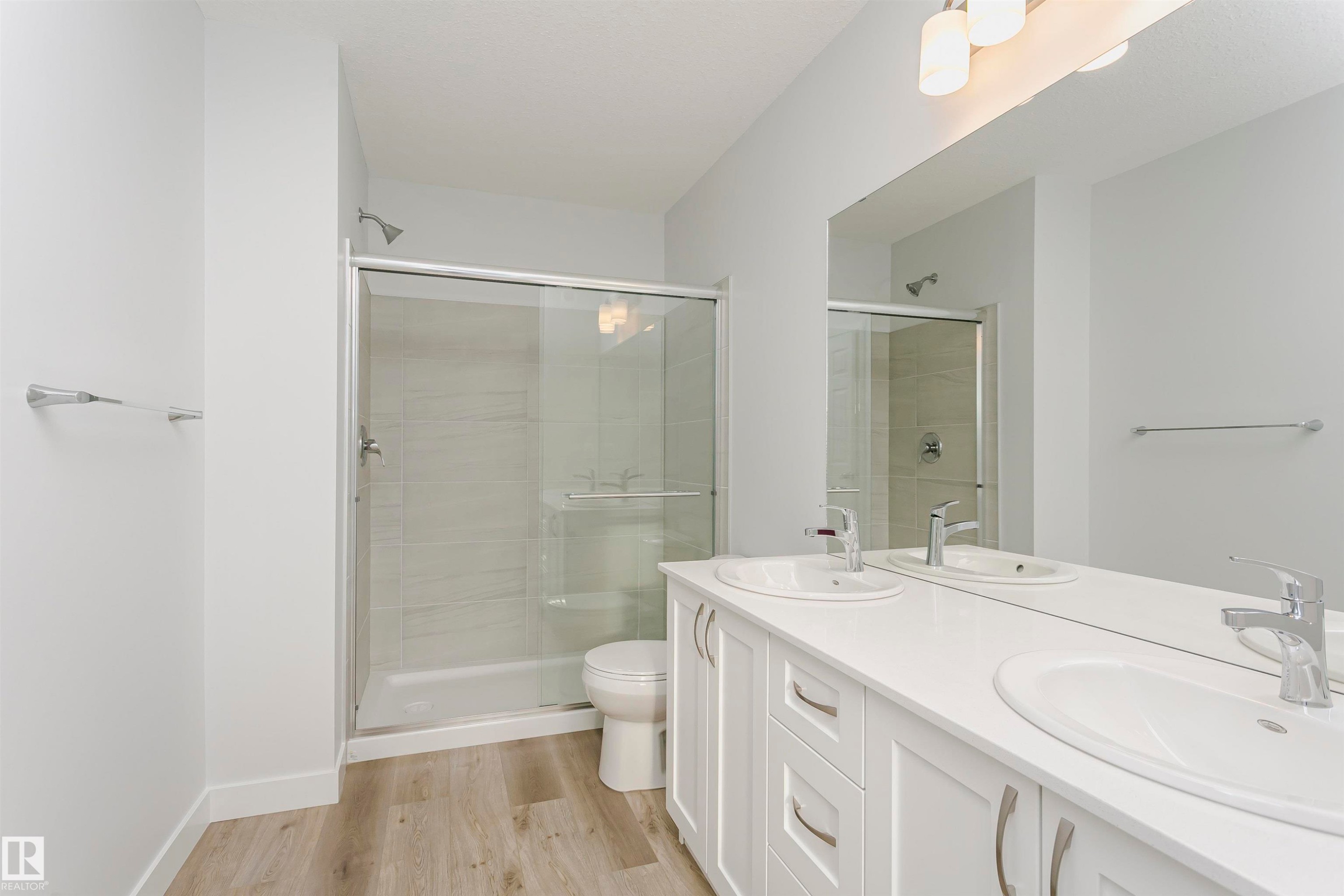 Bathroom featuring a double vanity with white cabinetry and integrated sinks, a full-width mirror, and wood-finish flooring - 9564 Carson Bend Bend, Edmonton, AB - Indoor Photo Showing Bathroom