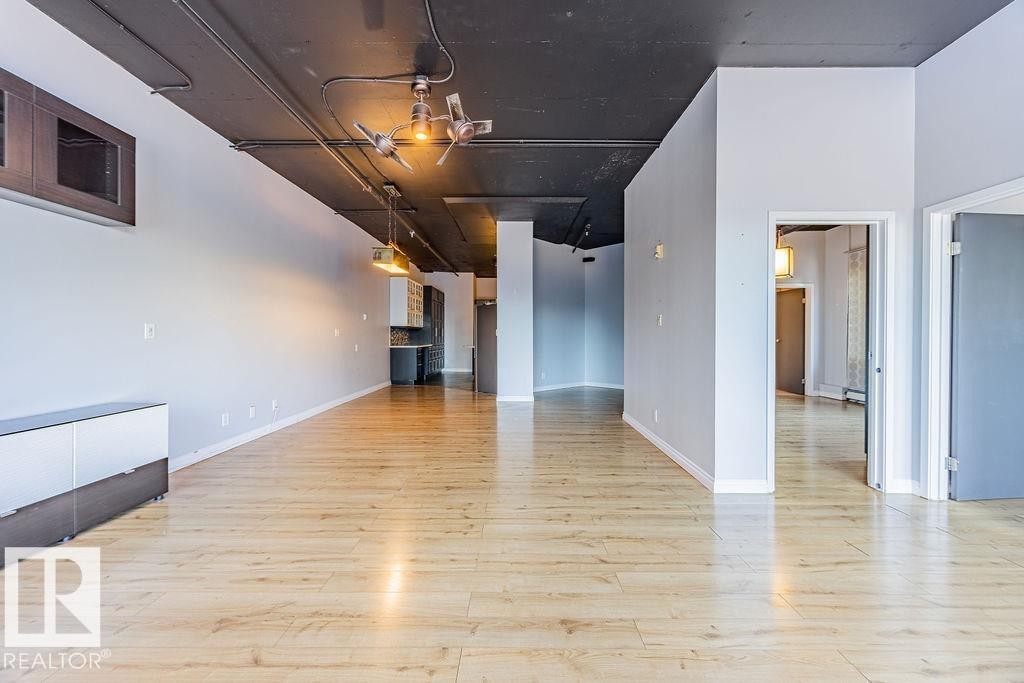 Expansive open-concept room featuring light wood-finish flooring, a dark exposed ceiling, and track lighting - 303 10179 105 Street, Edmonton, AB