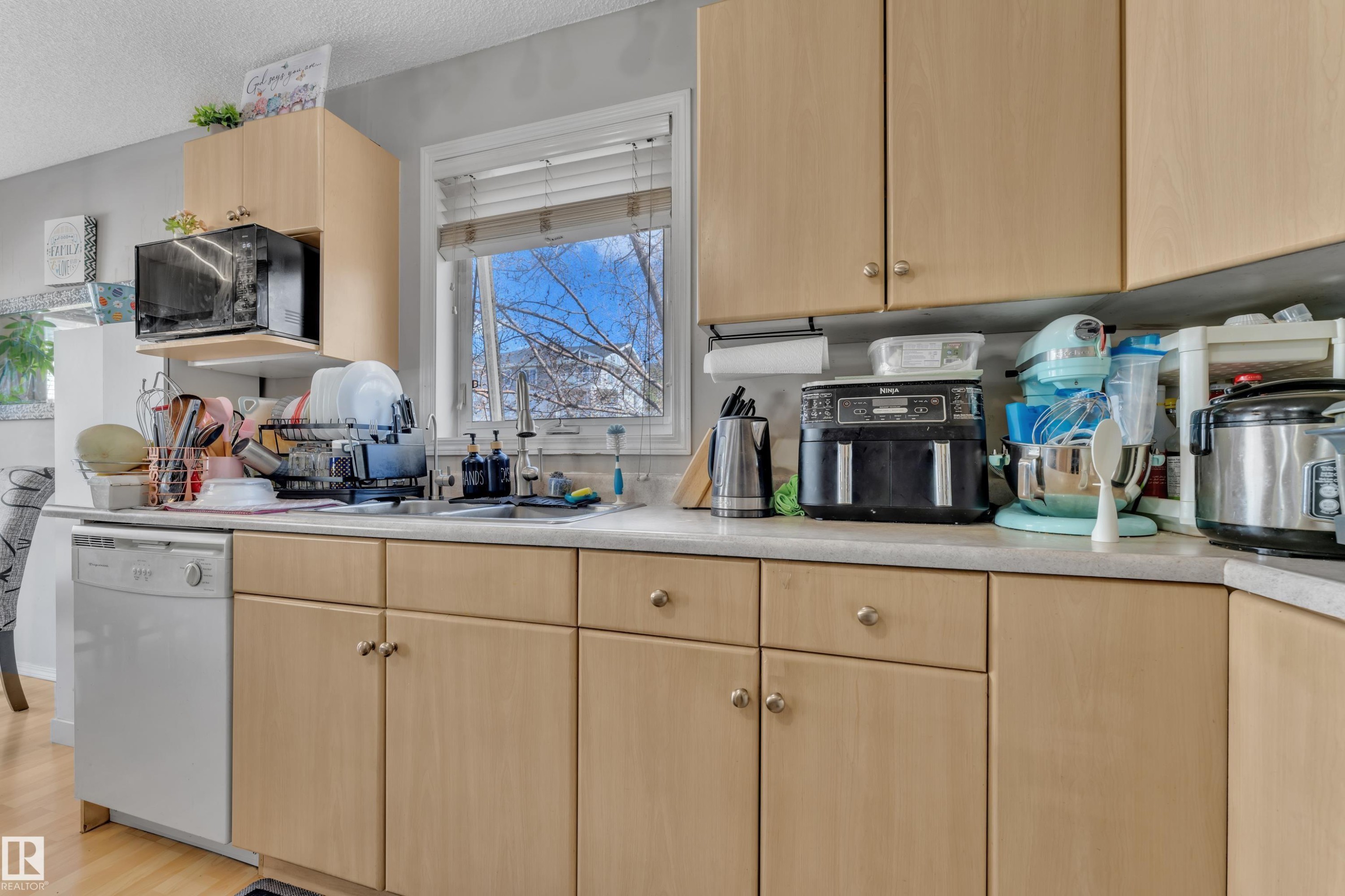 Kitchen featuring extensive wood-finish cabinetry, light-toned countertops, and a built-in dishwasher - #64 4350 23 St Nw, Edmonton, AB - Indoor Photo Showing Kitchen