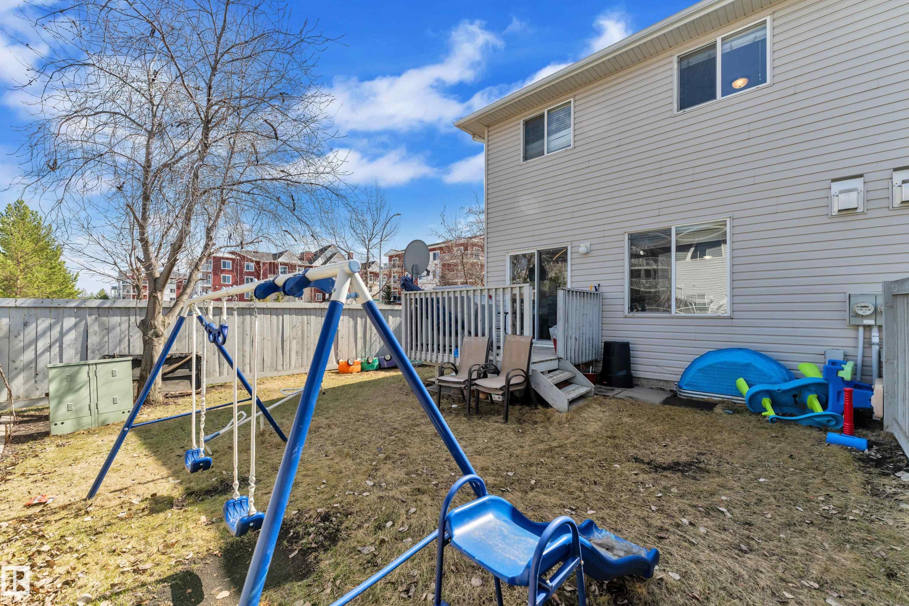Rear exterior featuring horizontal siding, multiple windows, and a sliding glass door leading to a wooden deck - #64 4350 23 St Nw, Edmonton, AB - Outdoor