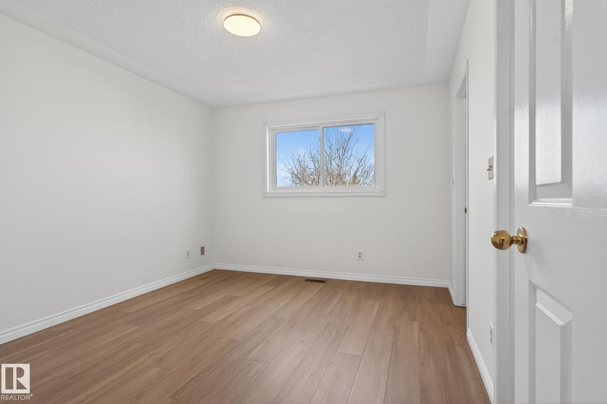 Bright room featuring wood-finish flooring, white baseboards, a single window, and a flush-mount ceiling light fixture - 8403 190 Street, Edmonton, AB - Indoor Photo Showing Other Room