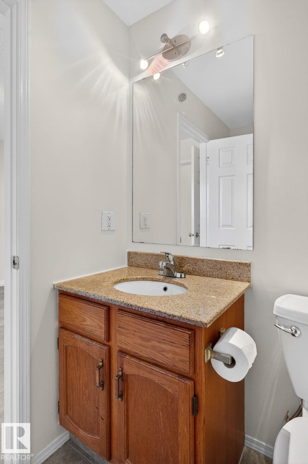 Bathroom vanity featuring a granite countertop, undermount sink, and wood-finish cabinetry with decorative hardware - 8403 190 Street, Edmonton, AB - Indoor Photo Showing Bathroom