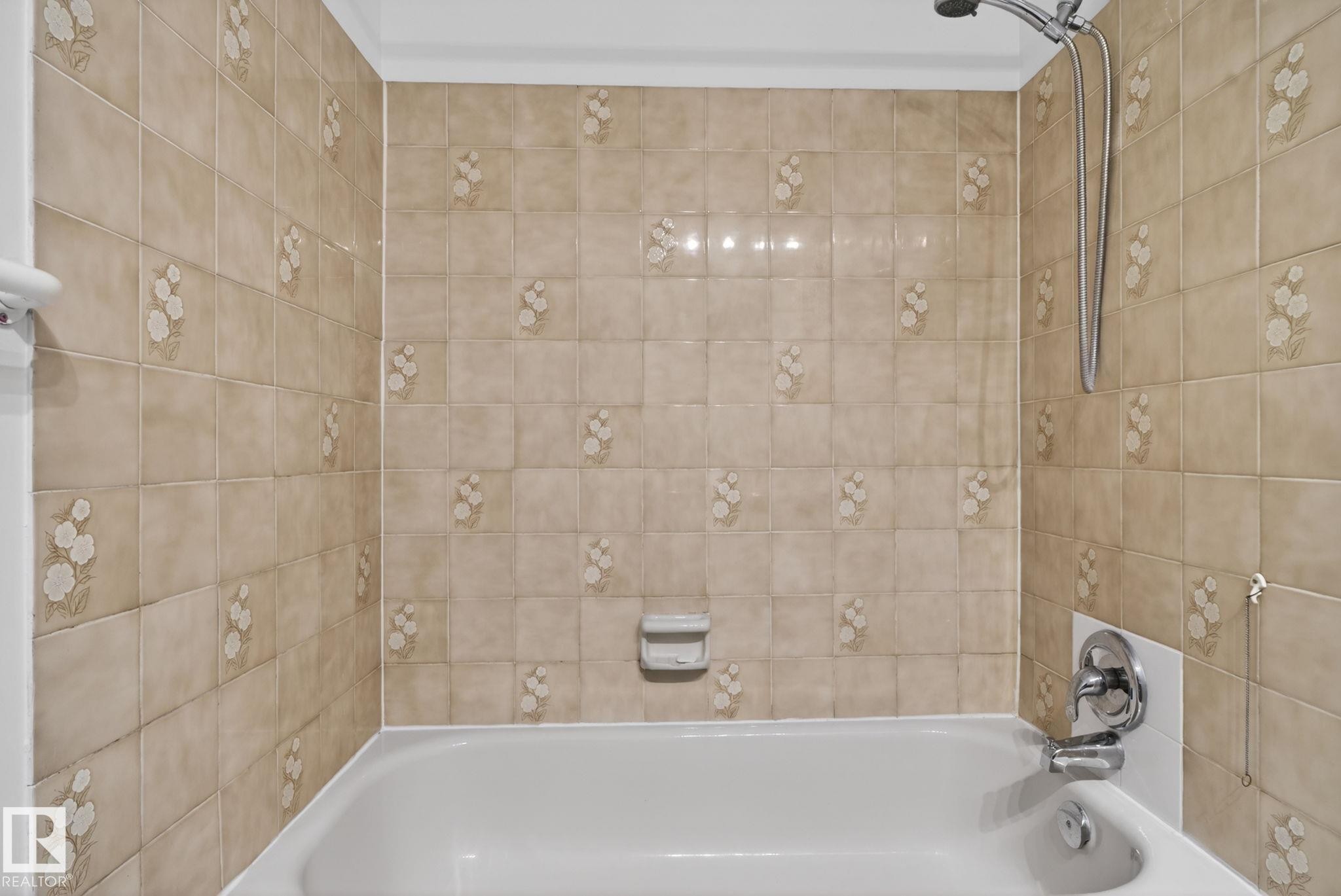 Alcove bathtub with a beige tiled surround featuring a floral pattern - 8403 190 Street, Edmonton, AB - Indoor Photo Showing Bathroom
