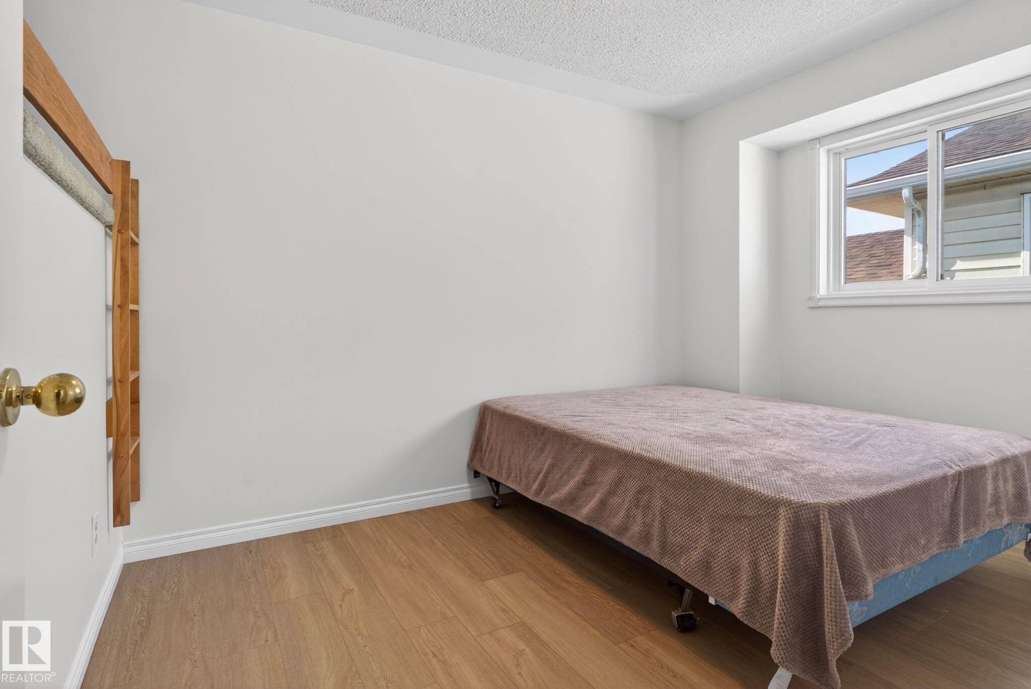 Bright interior room featuring wood-finish flooring, white baseboards, and a window with white trim - 8403 190 Street, Edmonton, AB - Indoor Photo Showing Bedroom